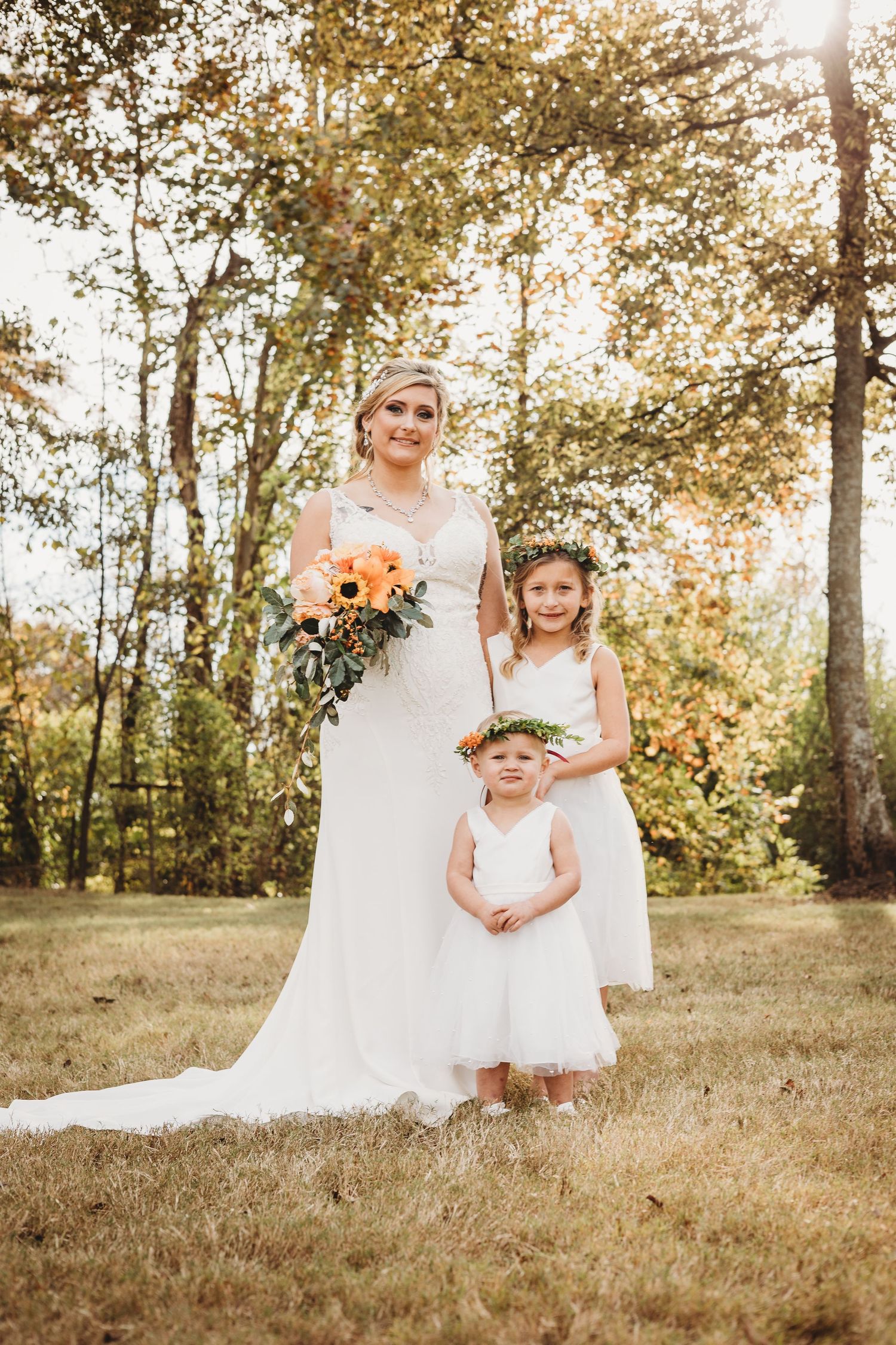 Wedding party and flower girl pose together in white dresses during outdoor autumn photoshoot.