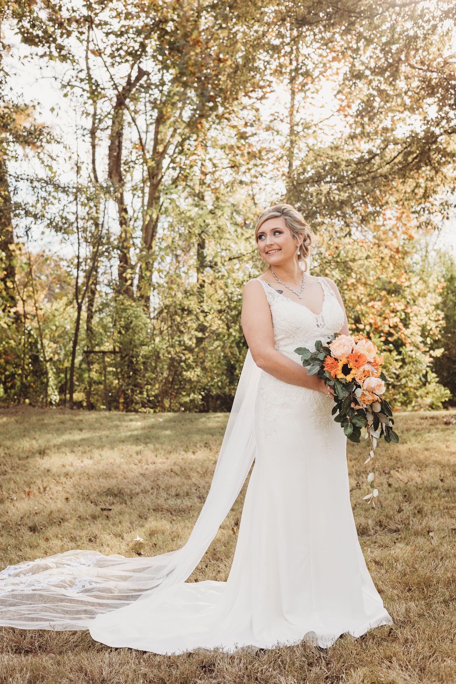 Long cathedral veil trailing behind white wedding dress in a scenic fall outdoor setting.