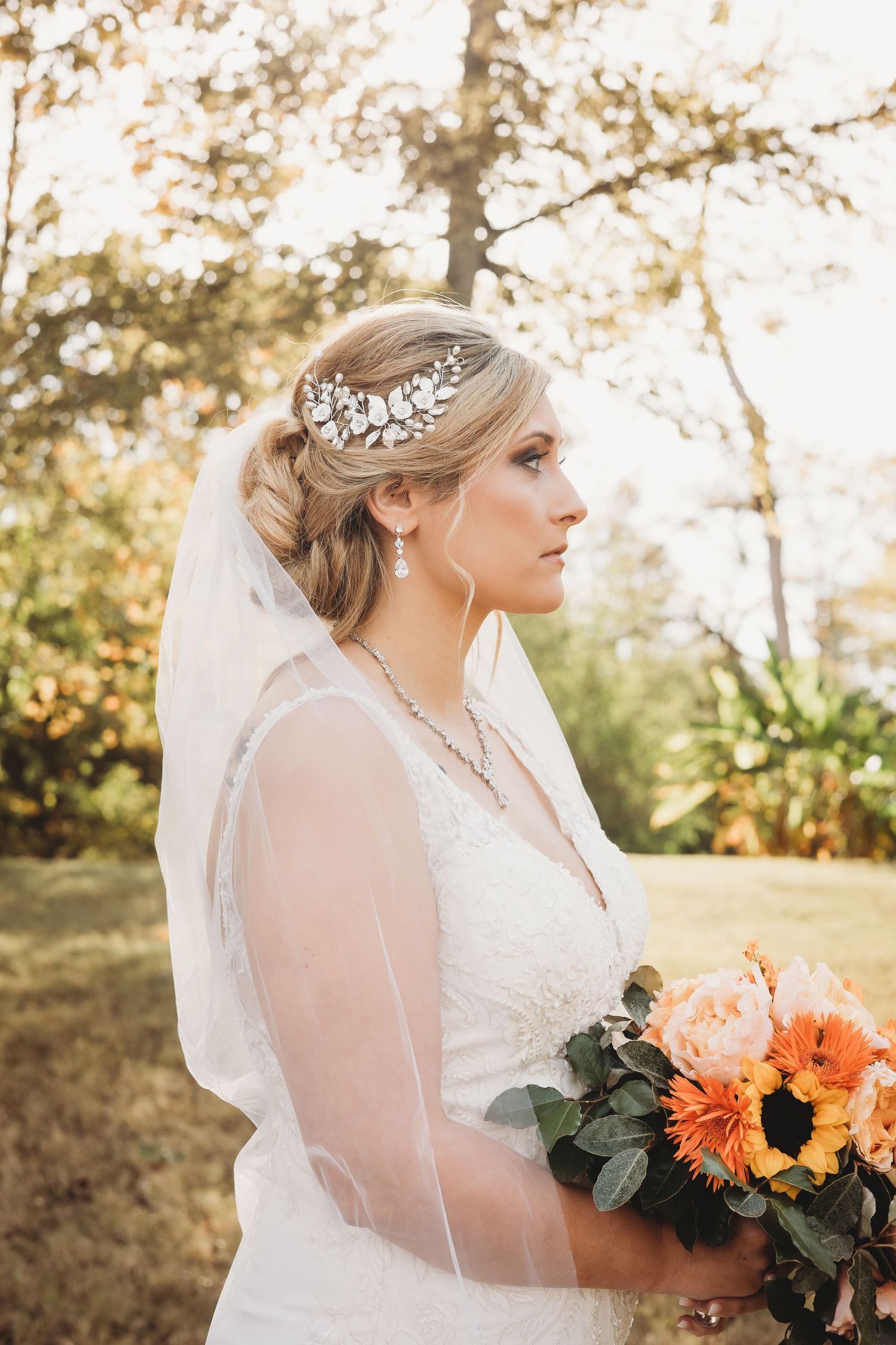 Bride holding orange and peach bouquet with sunflowers against autumn forest backdrop.
