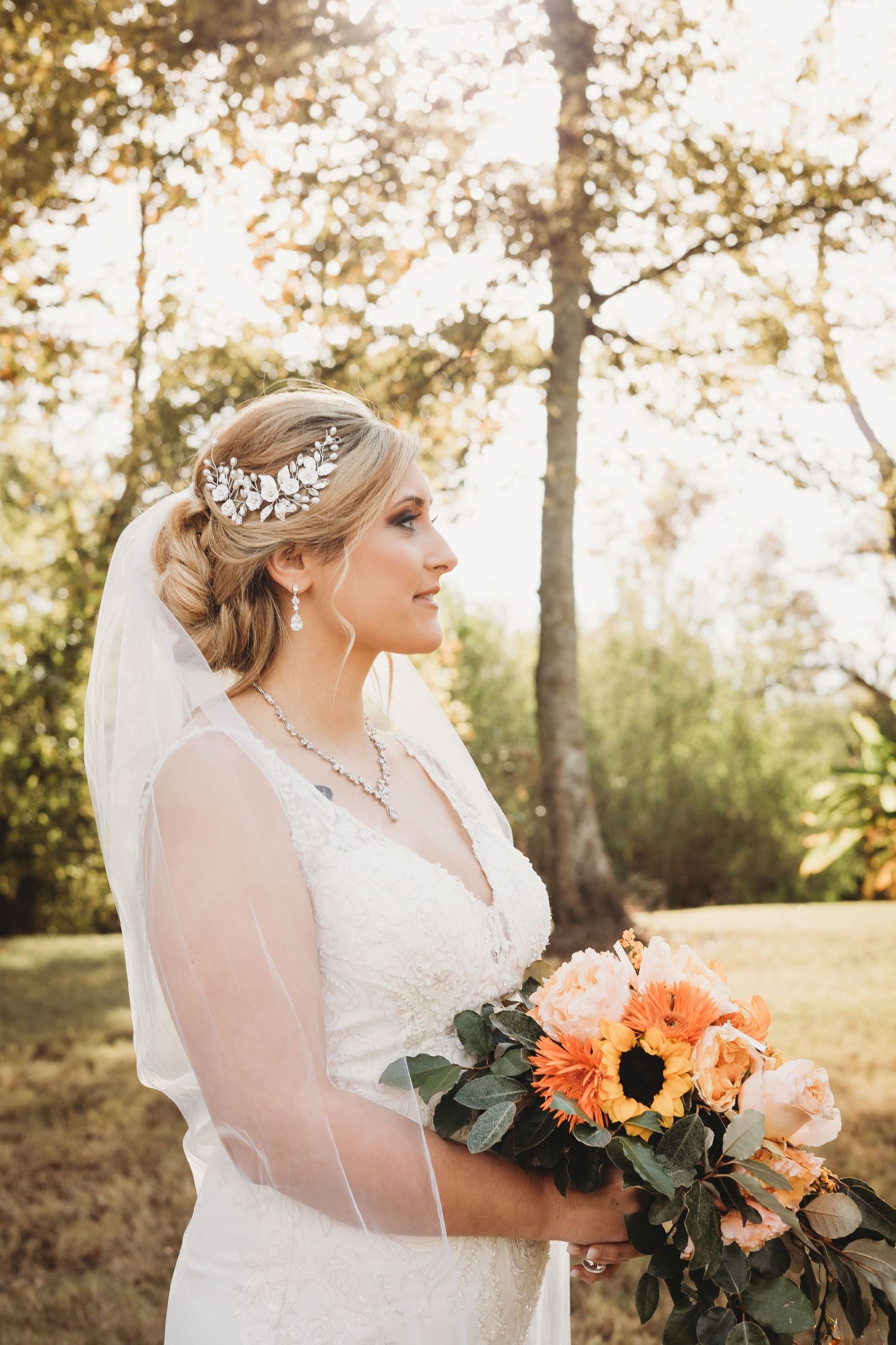 Bride with elegant updo and veil smiles while holding vibrant fall bouquet outdoors.
