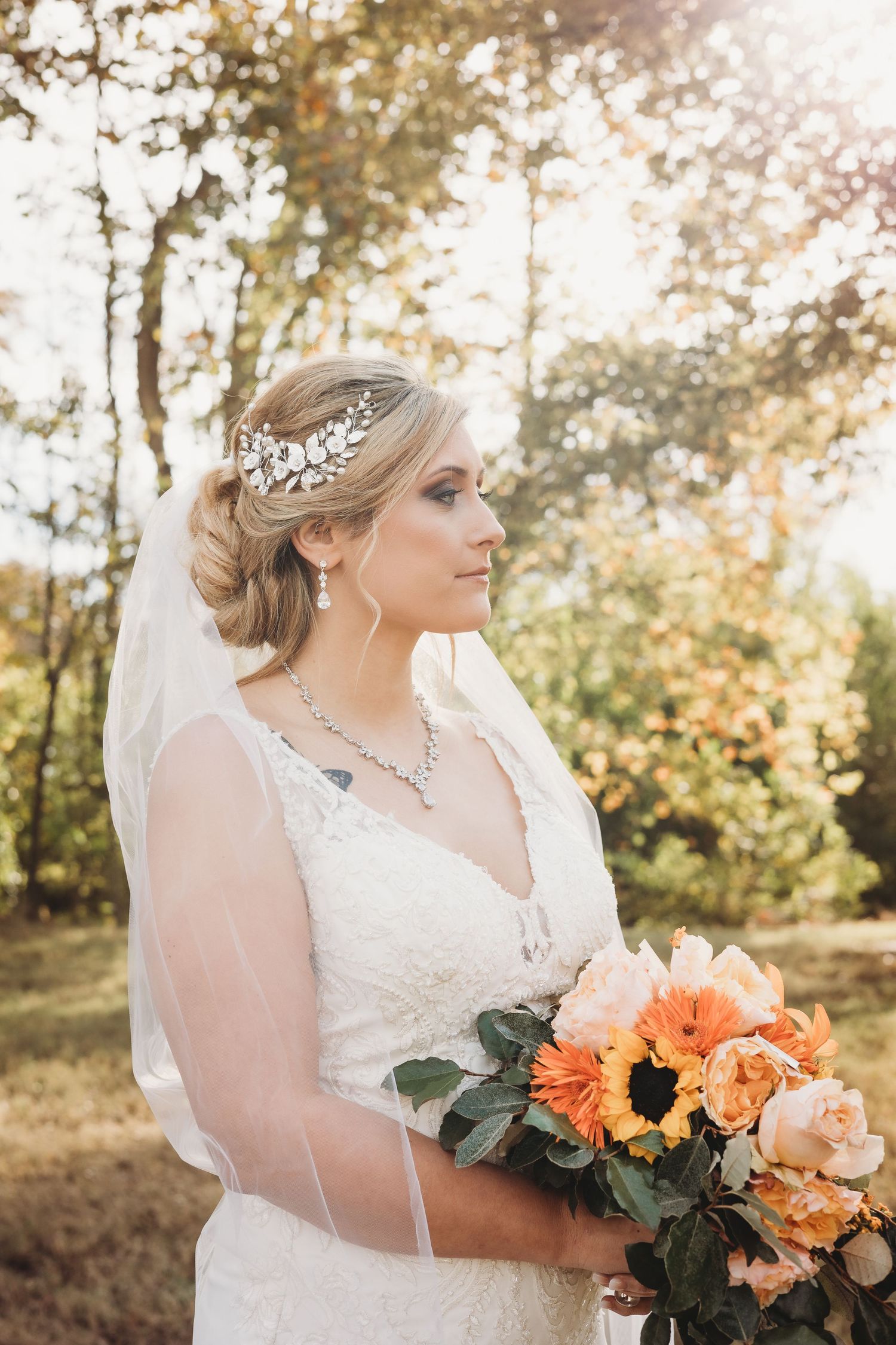 Bride in lace gown holds coral and orange bouquet during golden hour photo session.