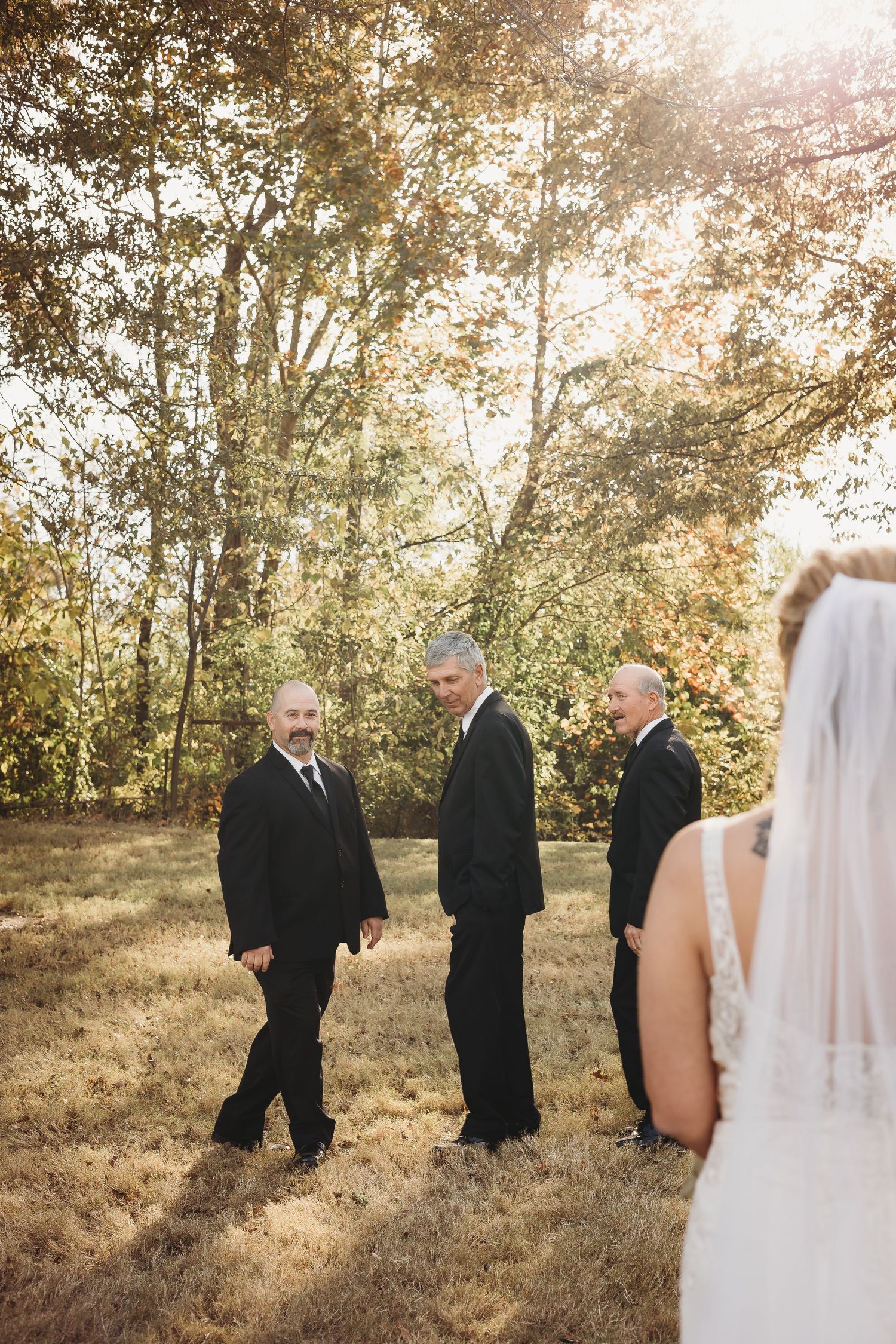 Wedding party in formal attire gathered outdoors during autumn sunset ceremony.