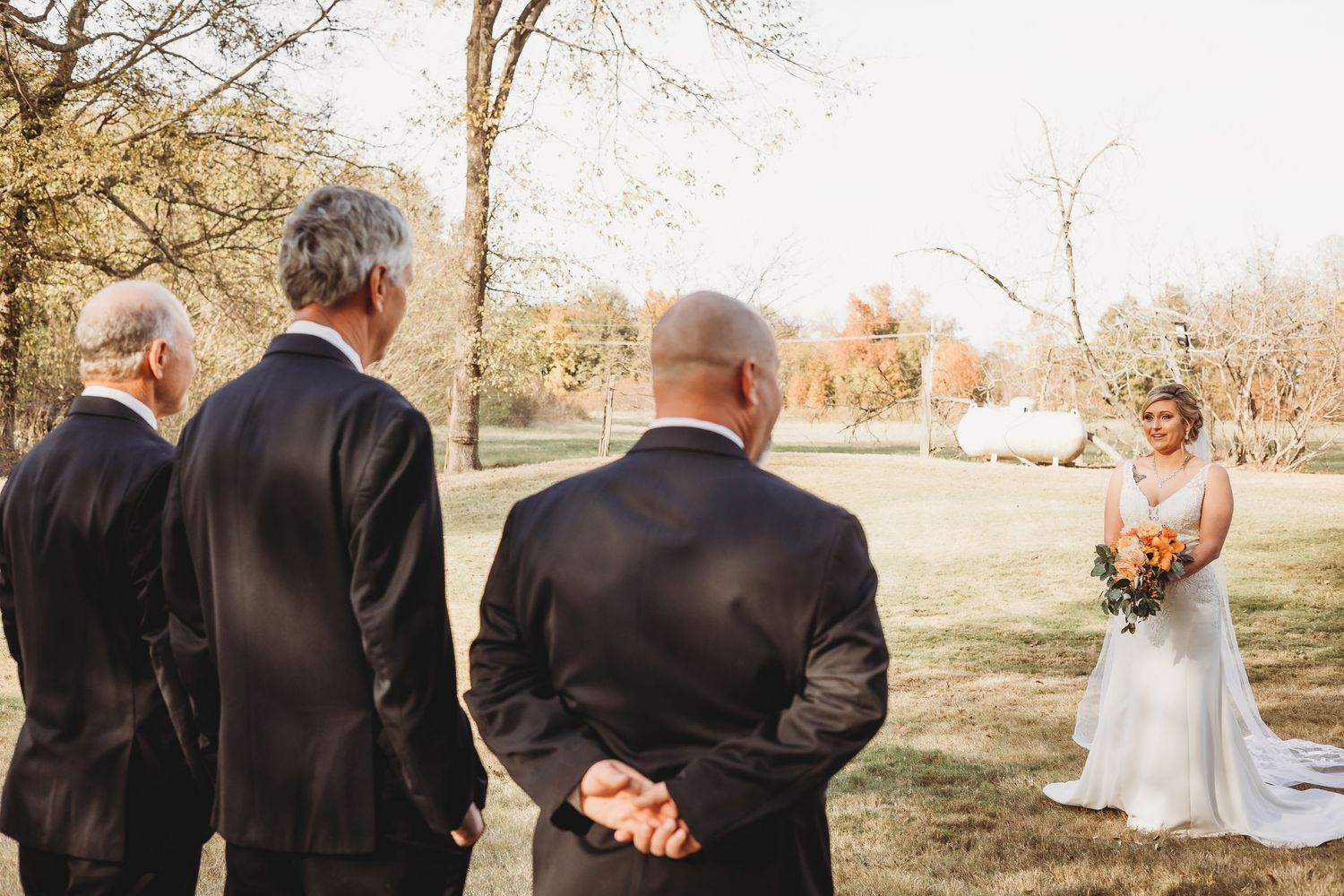 Wedding party members in formal attire gather outdoors for photos.