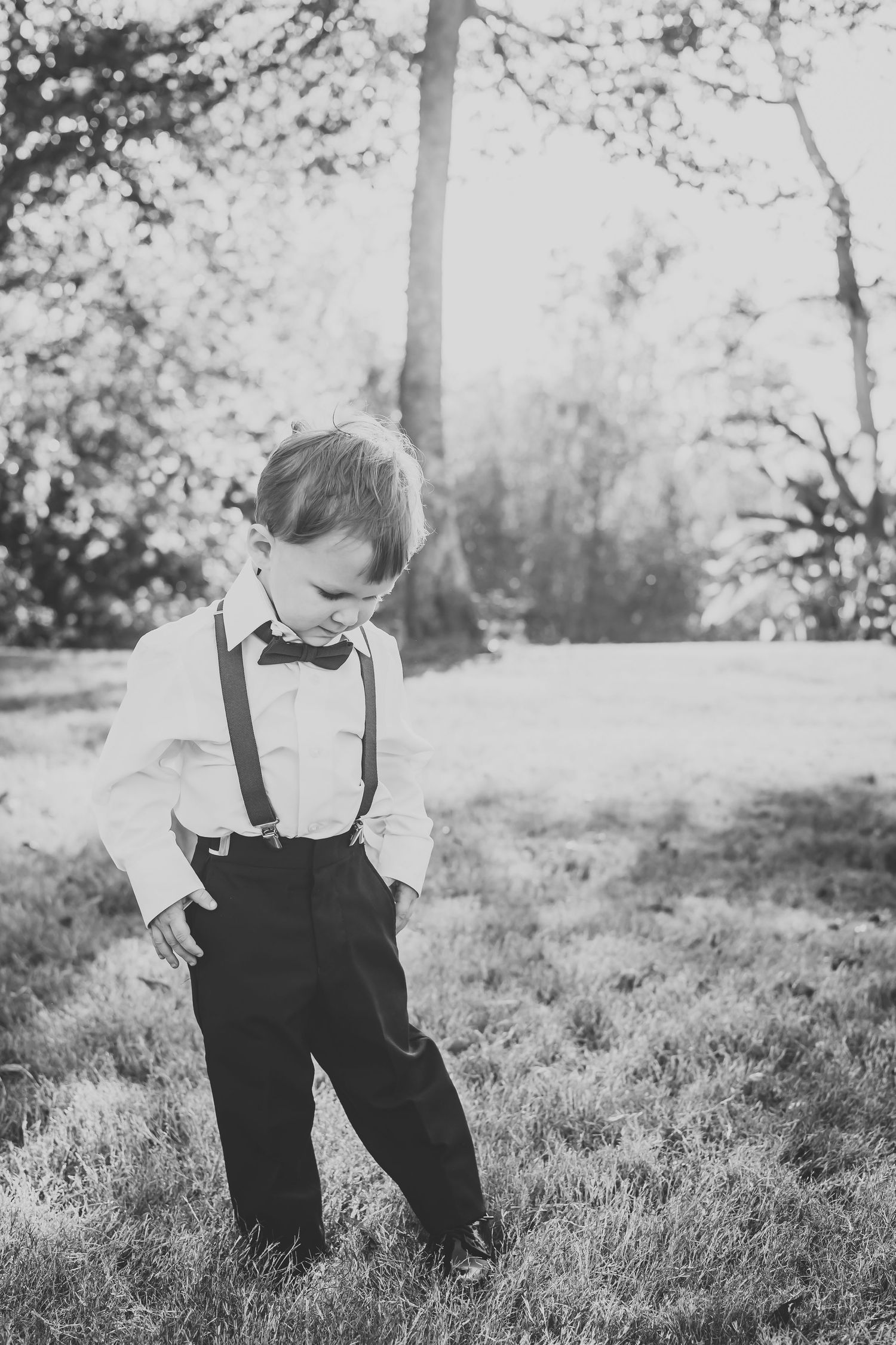 Black and white portrait of small child in suspenders playing in outdoor setting.