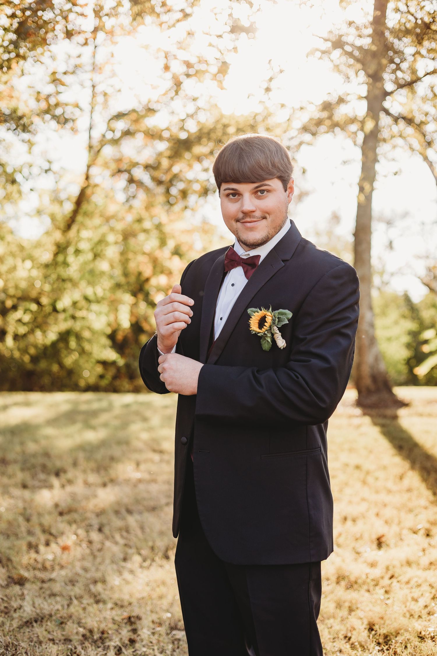 Person in formal black suit poses playfully in autumn outdoor setting.