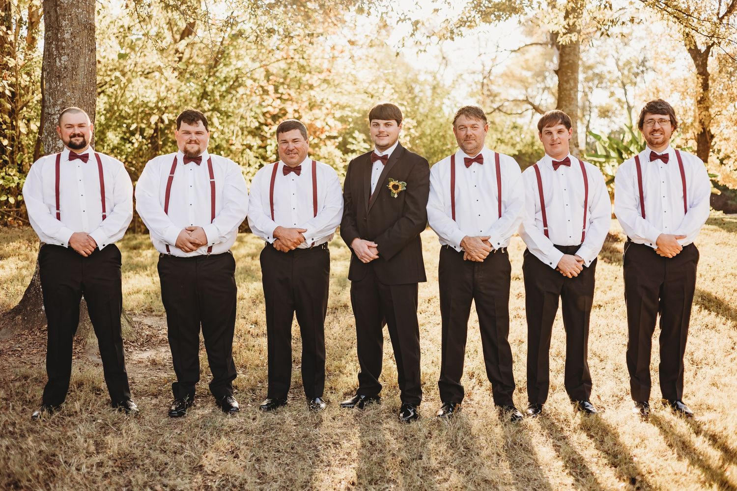 Large wedding party lined up outdoors wearing black and white formal attire with burgundy accents.