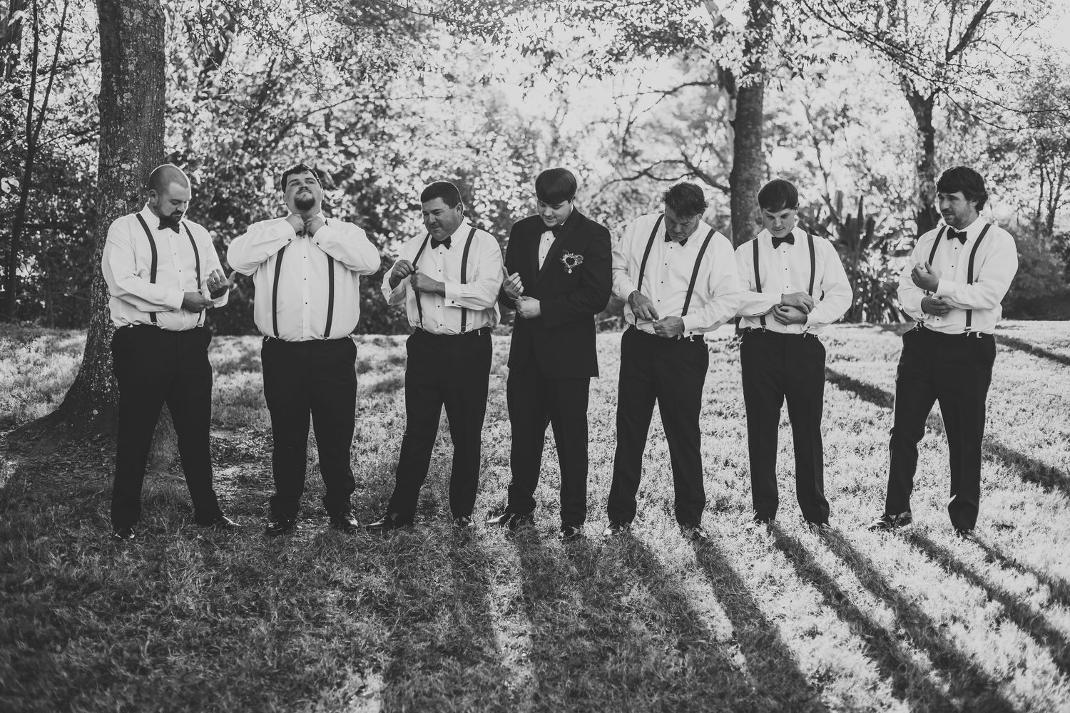 Black and white photo of groomsmen lined up outdoors casting long shadows in natural lighting.