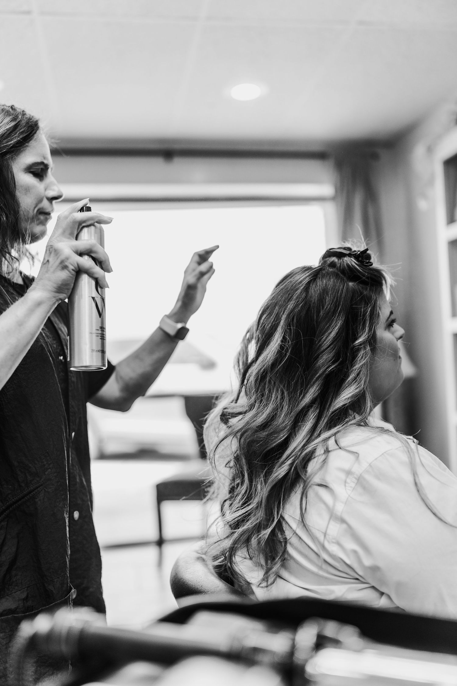 Hairstylist applying product while styling client's hair in black and white.
