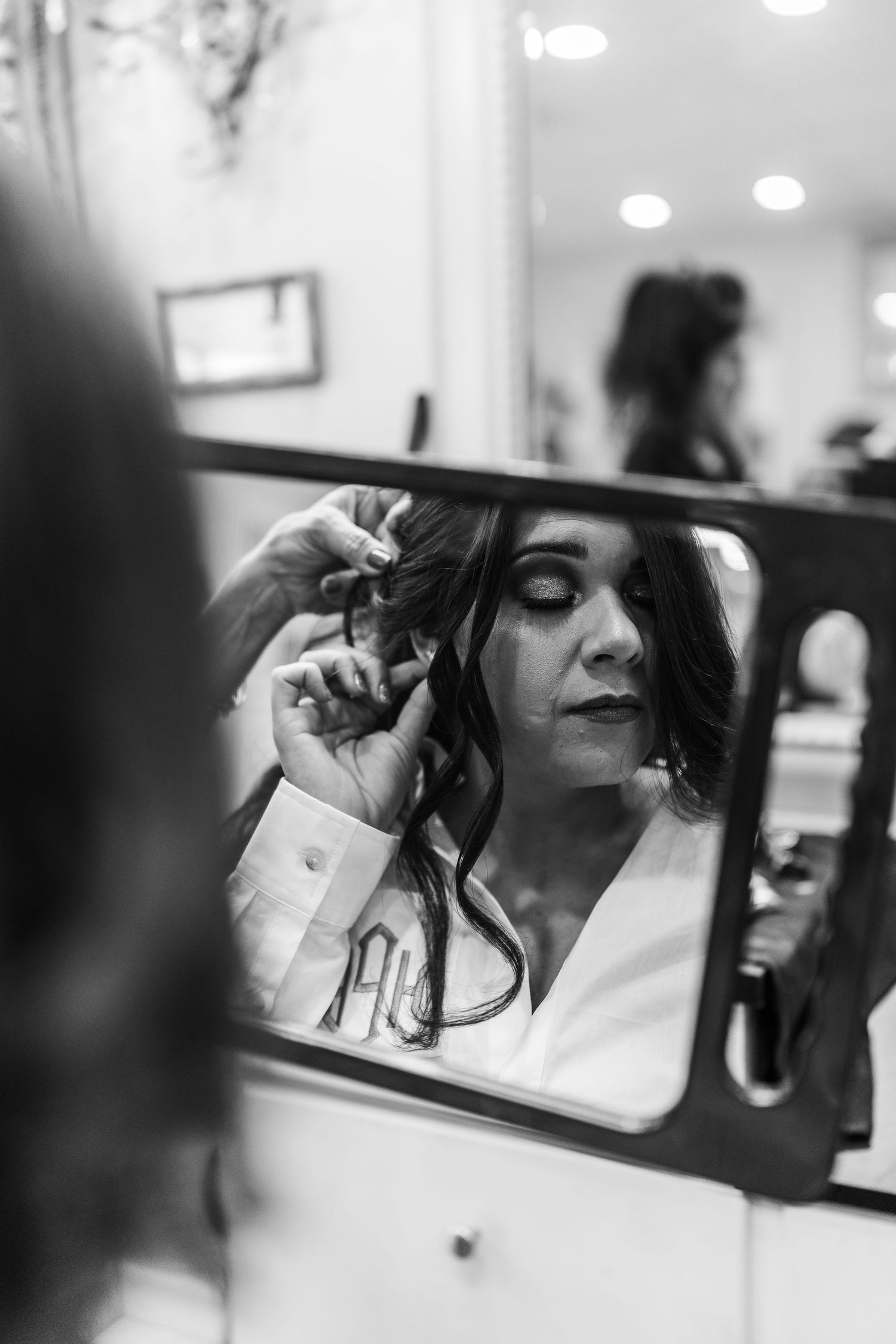 Black and white reflection of makeup application in a beauty mirror.