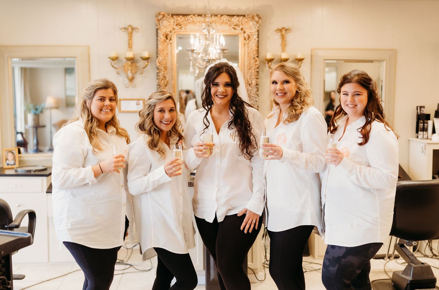 Friends in coordinated outfits pose playfully together in an elegant room with chandeliers.