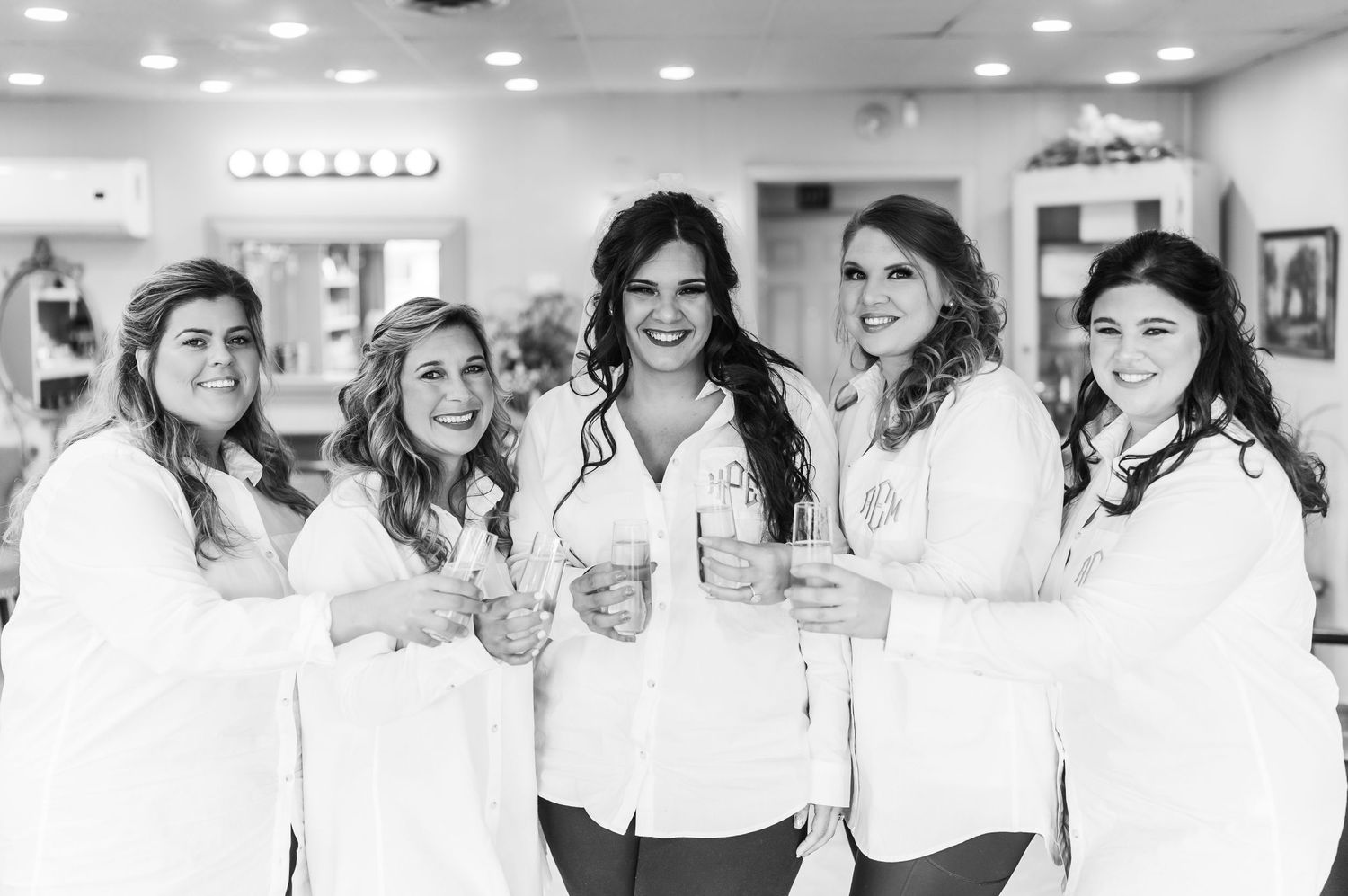Group photo of bridesmaids wearing white button-down shirts in a bright indoor space.