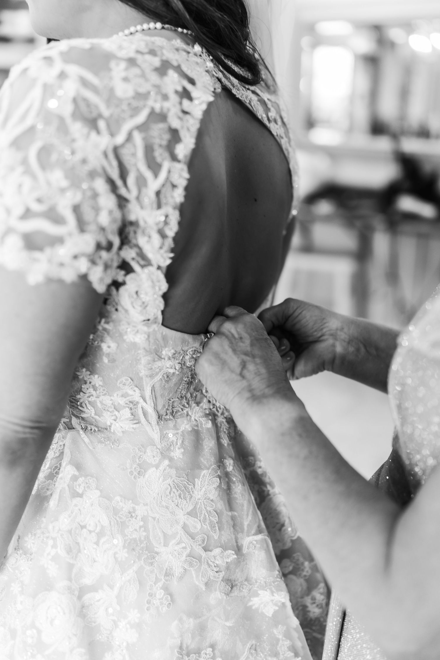 Black and white image showing the intricate back detail of a wedding gown being fastened.