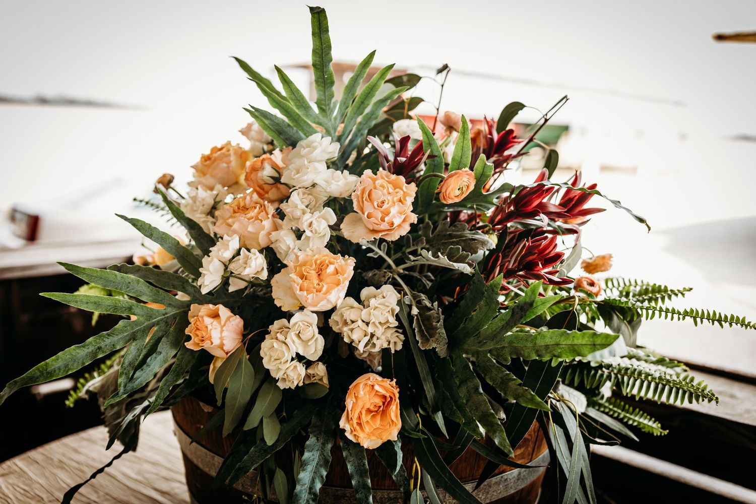 Peach-colored roses and greenery arranged in an elegant floral centerpiece on a rustic wooden surface.
