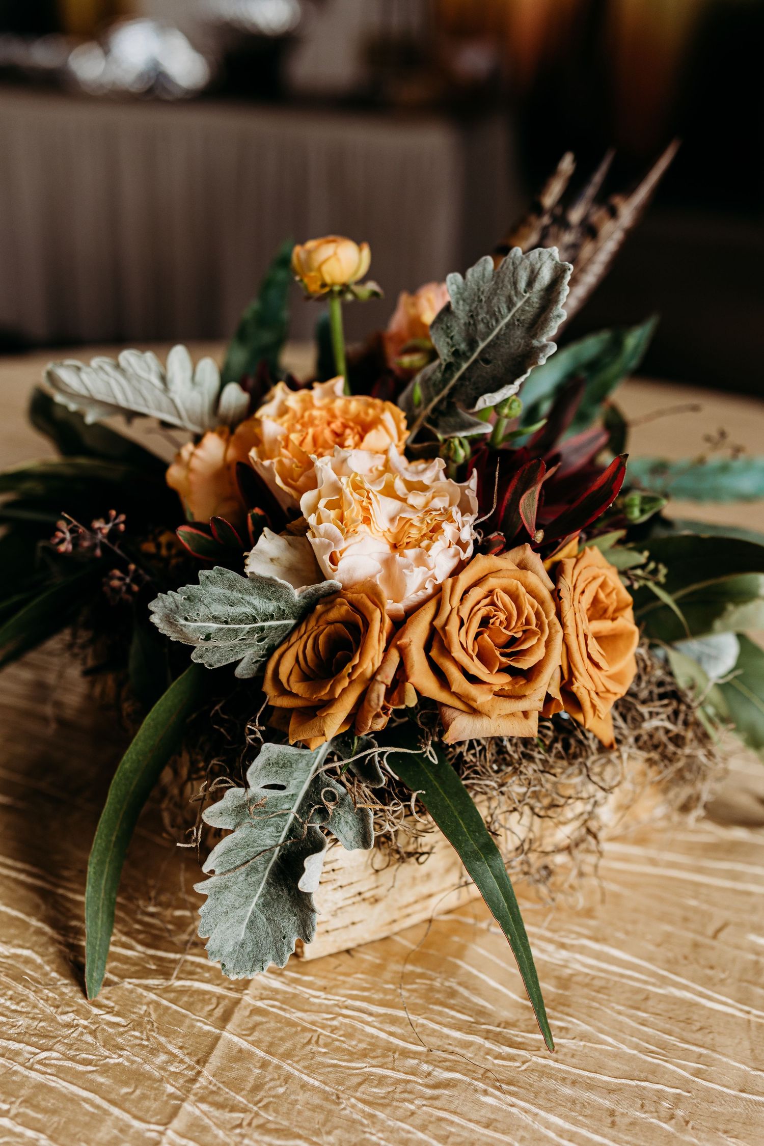 Close-up of peach roses with dusty miller leaves and greenery arranged on a light wooden surface.