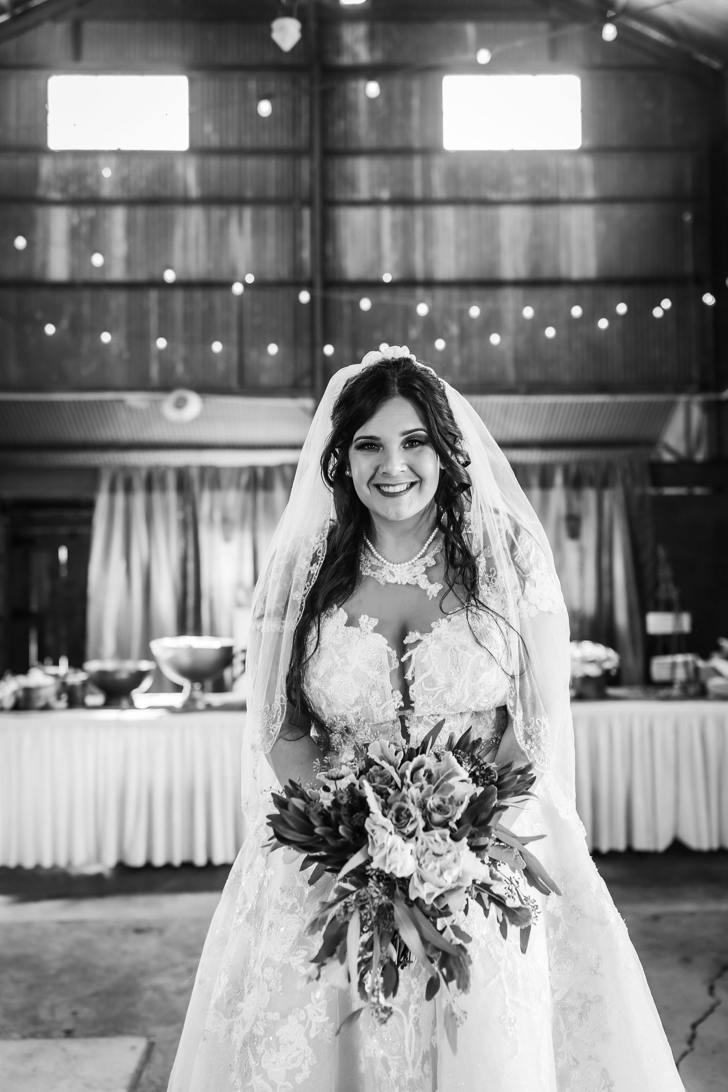 Black and white portrait of bride holding autumn bouquet in rustic barn setting.