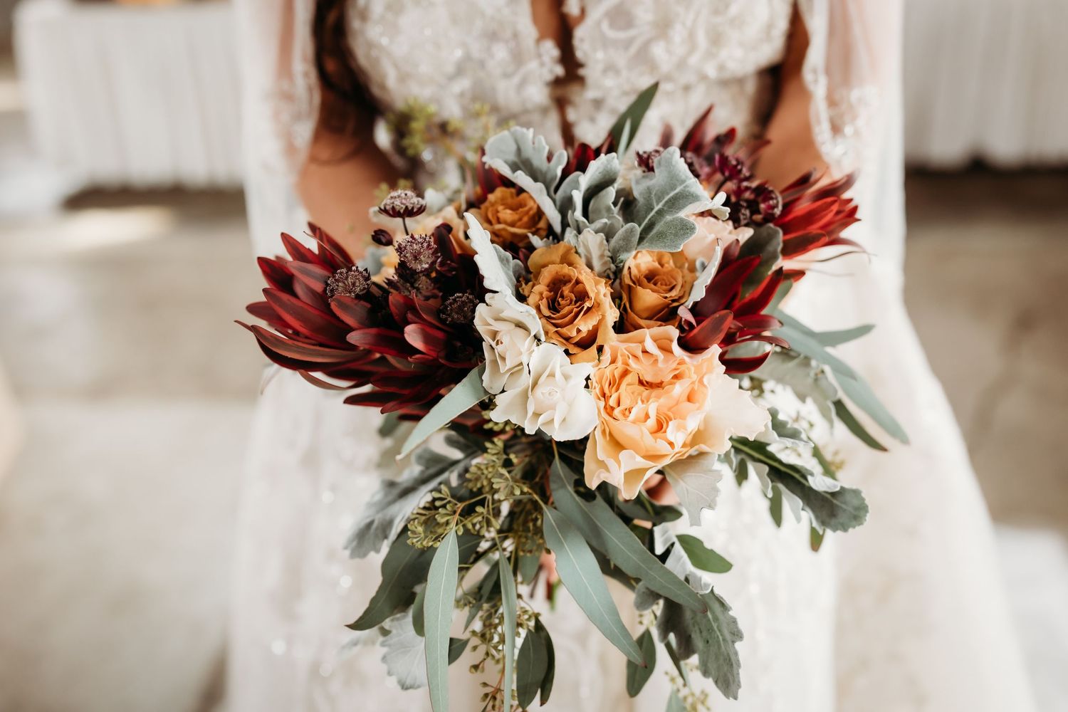 Detail shot of autumn wedding bouquet featuring deep red flowers and sage green foliage.