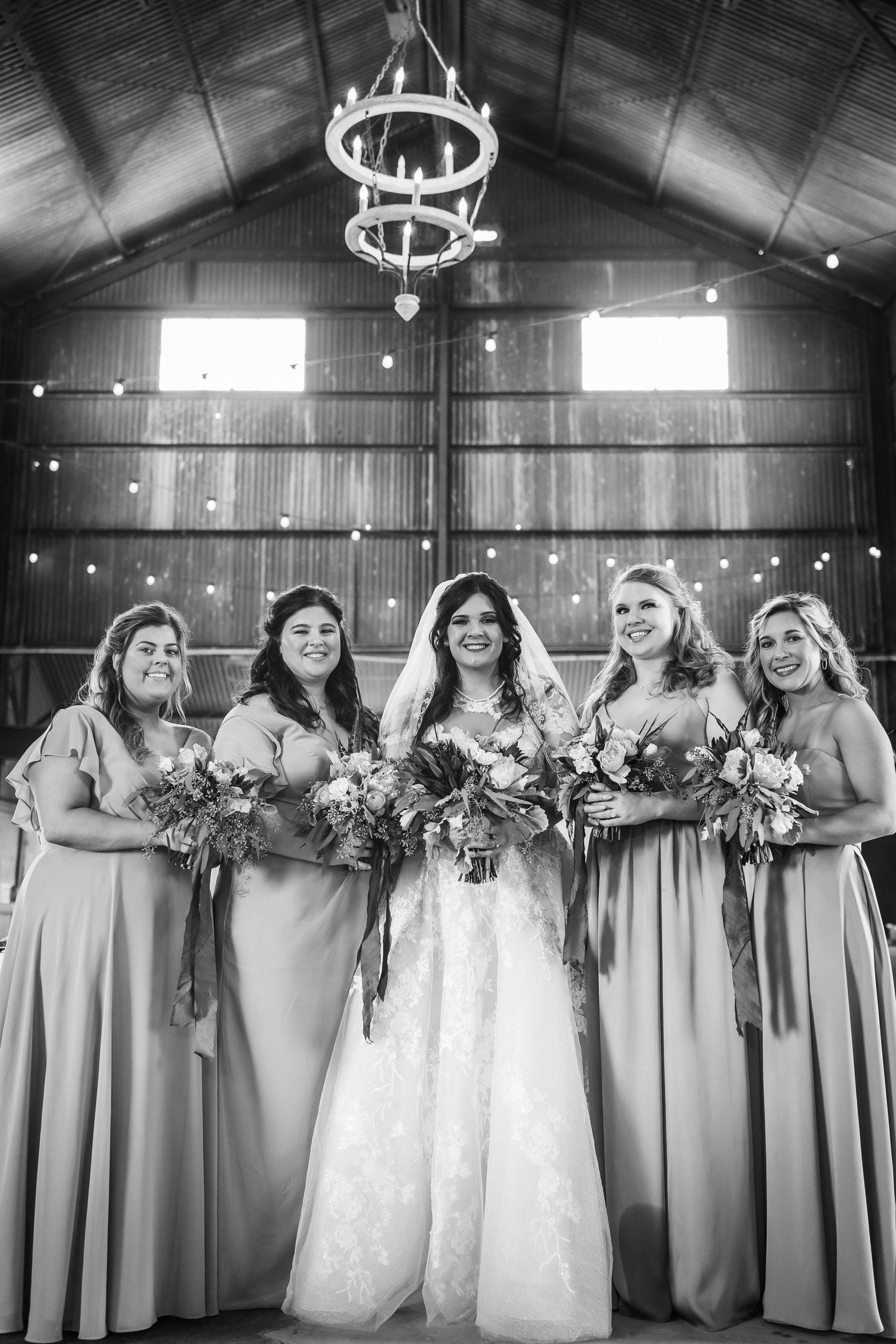 Black and white photo of bridal party in long dresses lined up in rustic barn venue.