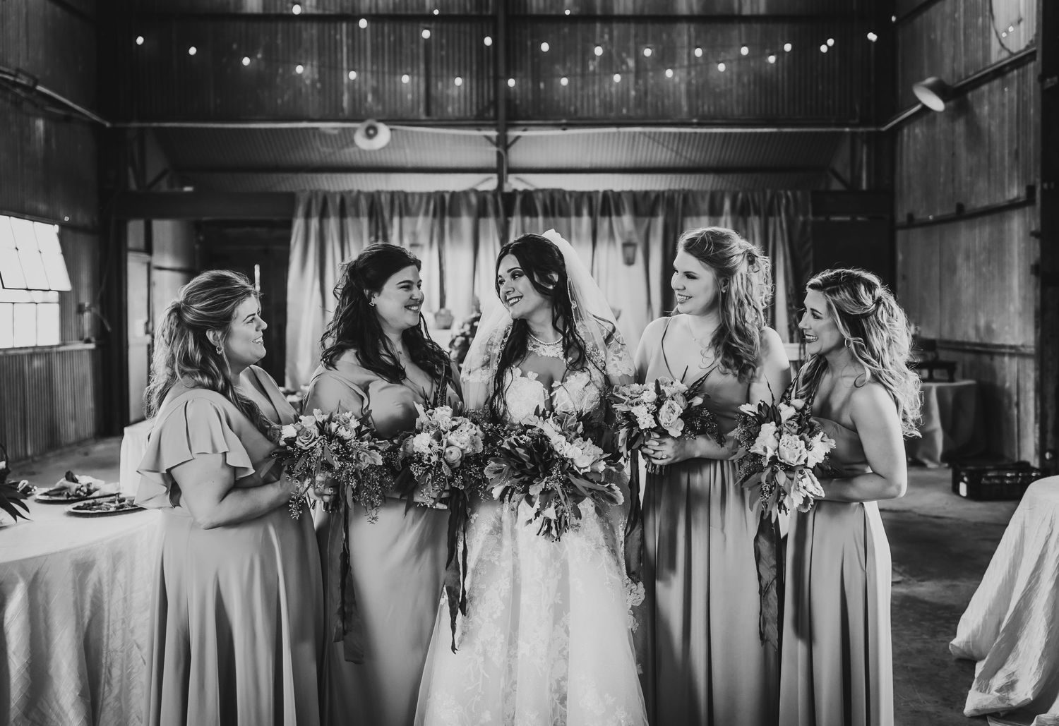 Black and white panoramic shot of wedding party lined up in rustic barn venue.