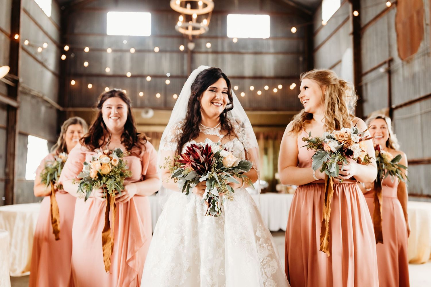 Candid celebration moment of bridal party in peach dresses inside rustic barn venue.