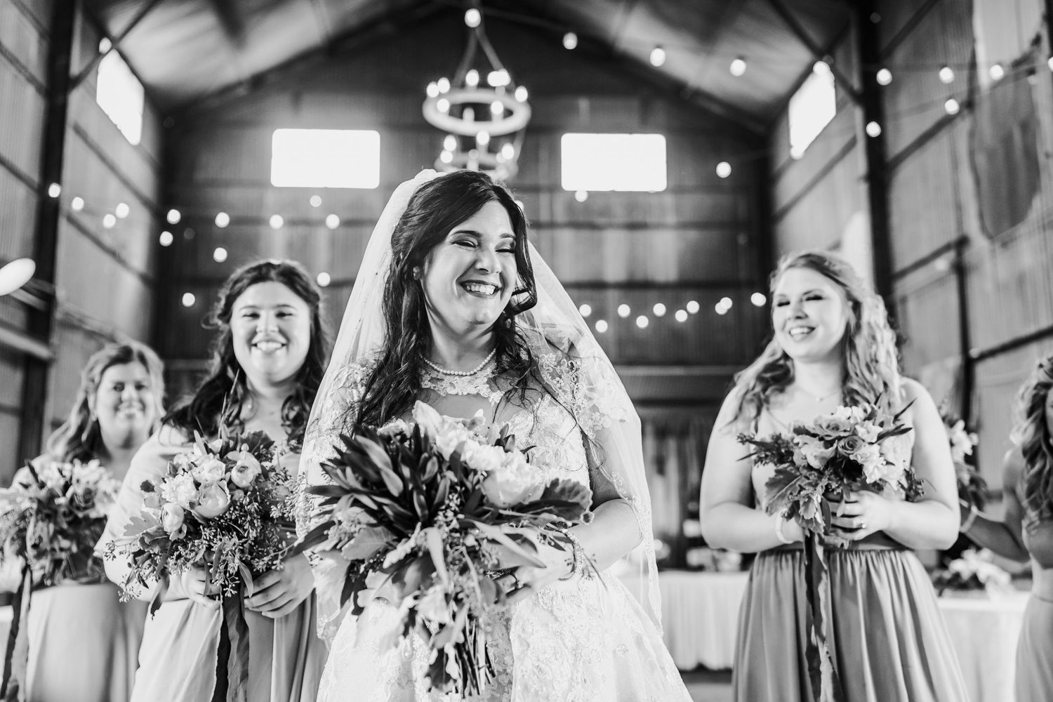 Black and white capture of joyful wedding party celebration in barn setting.