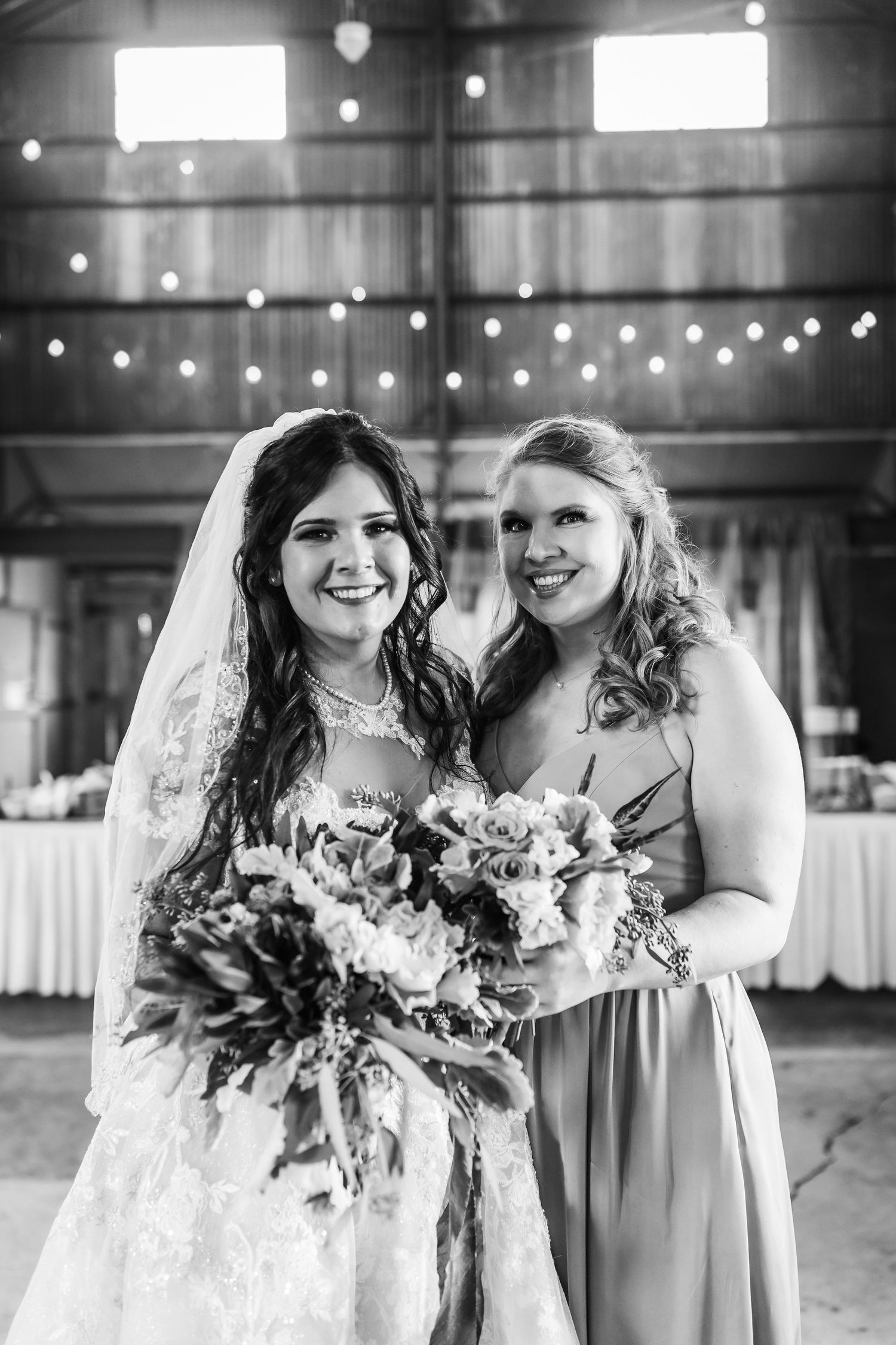 Black and white portrait of wedding party with bouquets in rustic barn setting.