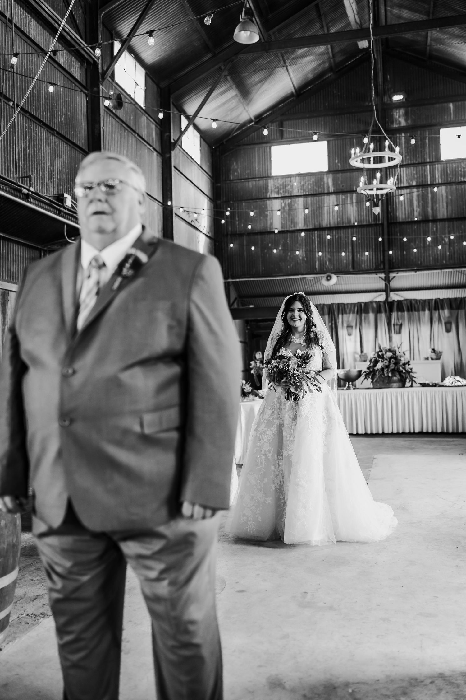 Black and white photo of wedding venue interior with man in suit and string light decorations.
