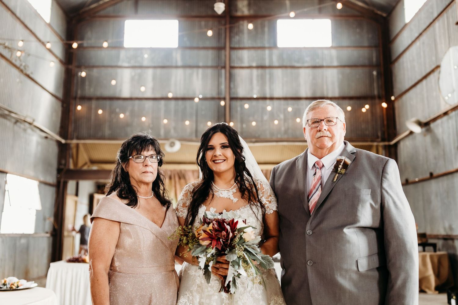 Wedding party members gather in rustic barn venue with string lights and wooden details.