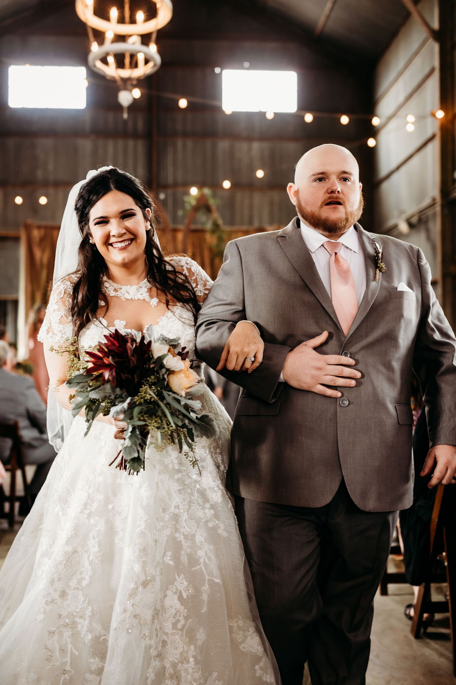 Newlyweds share laughter while walking down the aisle in an industrial wedding venue.