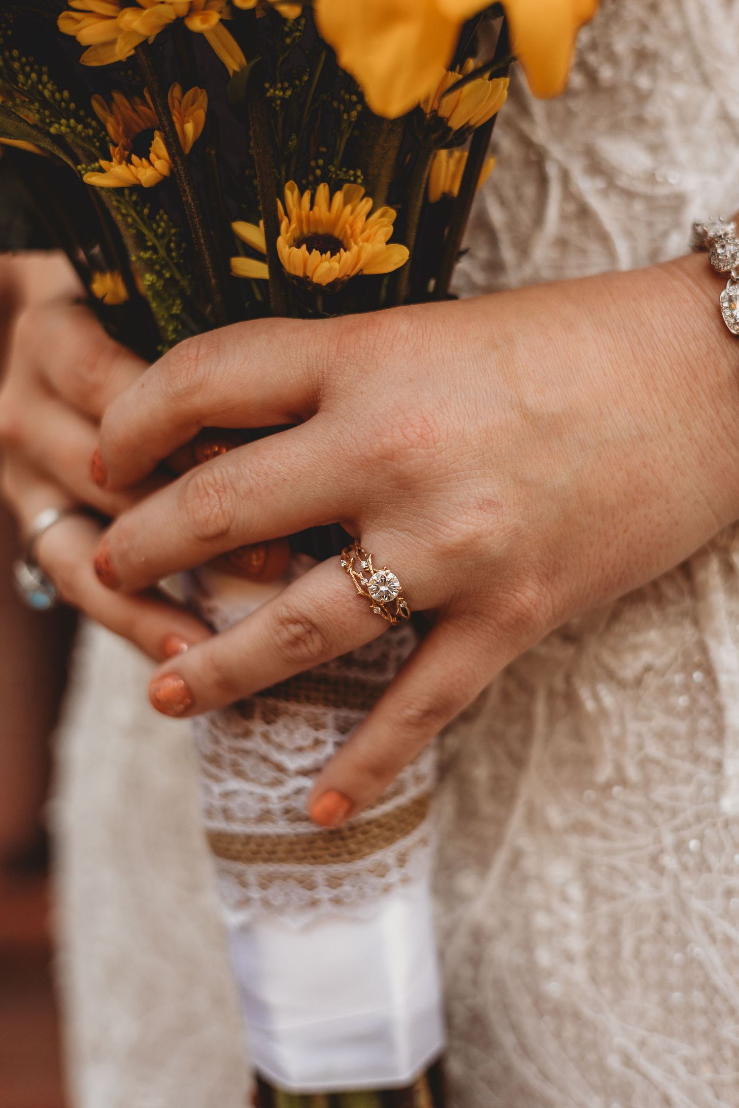Close-up of hands wearing delicate lace wedding dress details and jewelry.