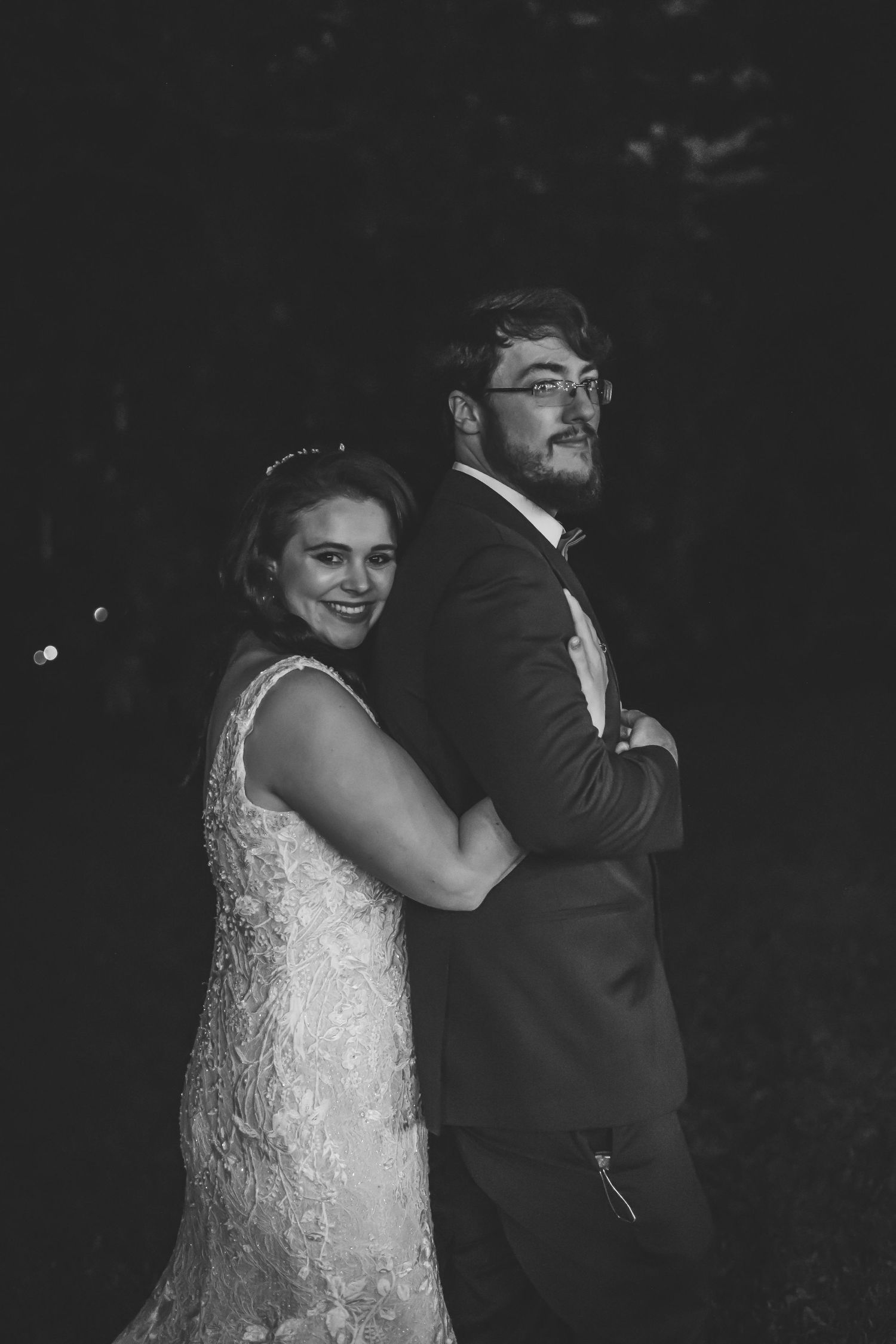 Black and white wedding photo showing couple embracing in evening lighting.