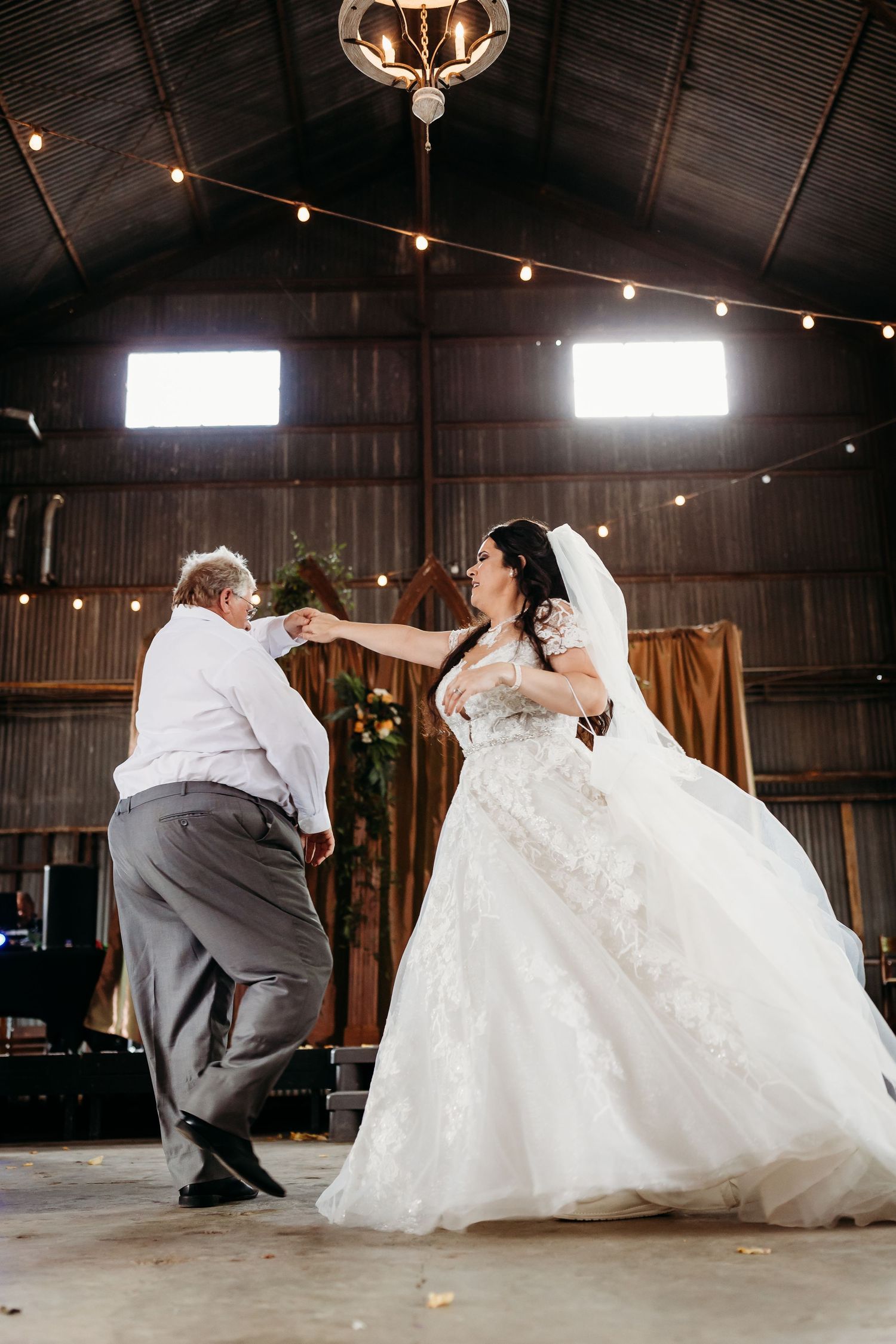 Couple performs choreographed first dance in rustic barn venue with string lights overhead.