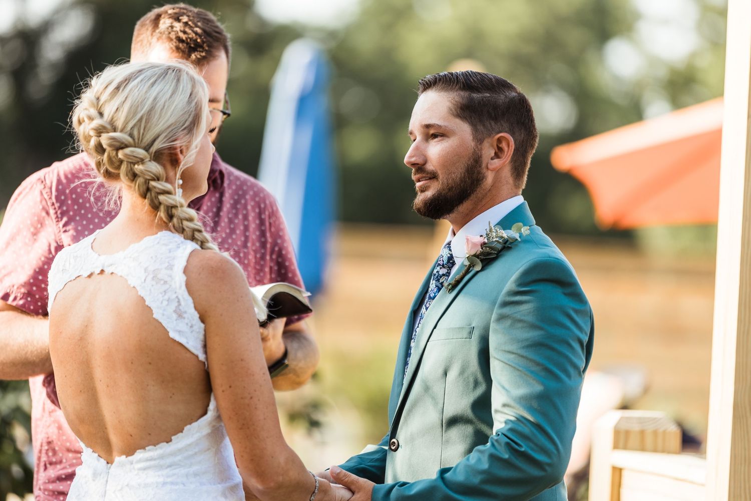 An outdoor wedding ceremony showing the bride's detailed lace back dress during the vows.