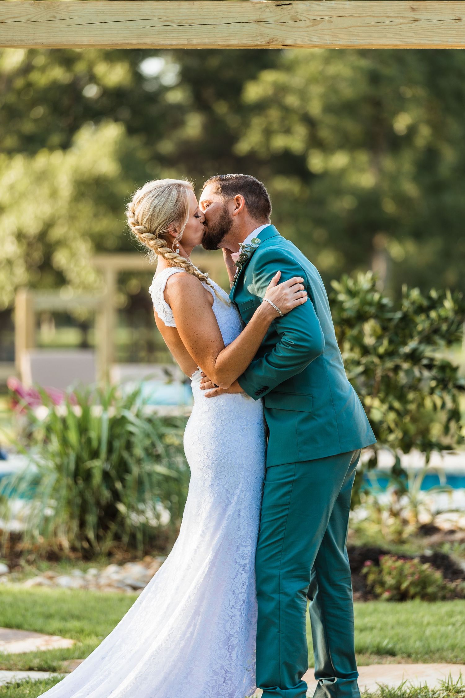 A joyful first kiss between newlyweds in a garden setting with greenery backdrop.
