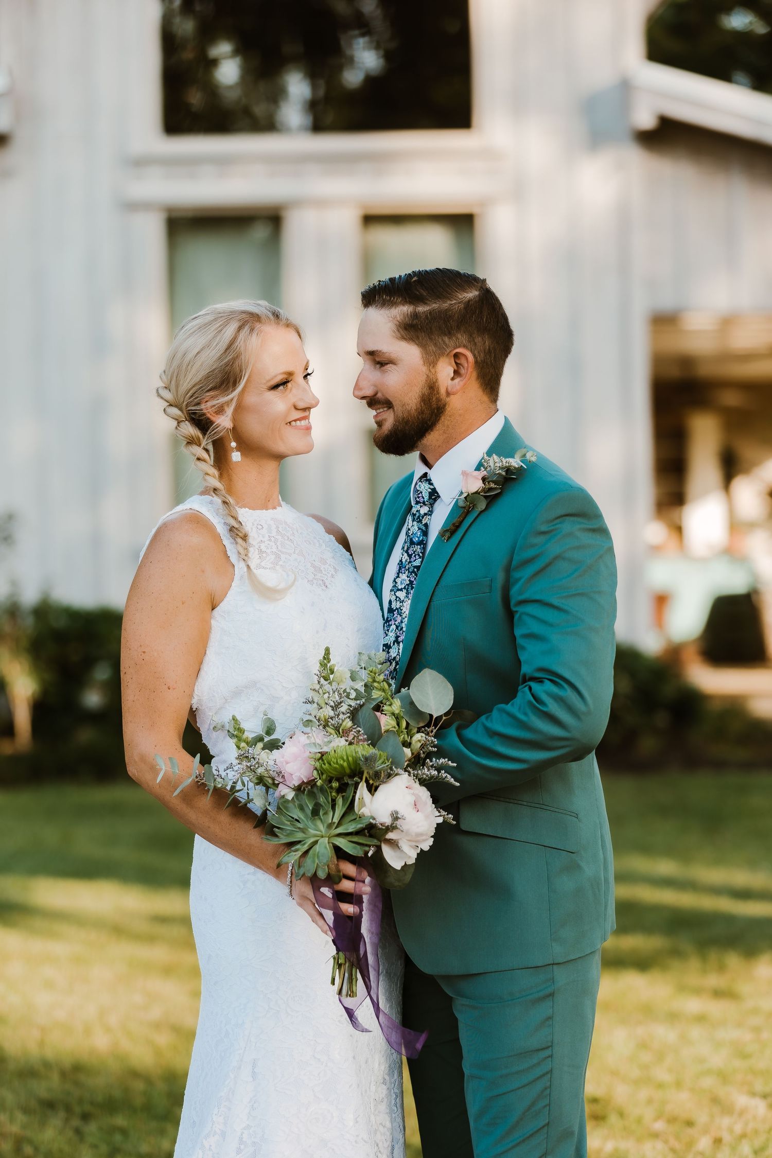 A candid wedding moment shows a couple sharing a laugh in front of a white barn building.