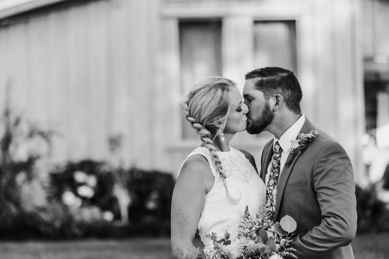 An intimate black and white wedding photo shows a couple sharing a tender moment outdoors.