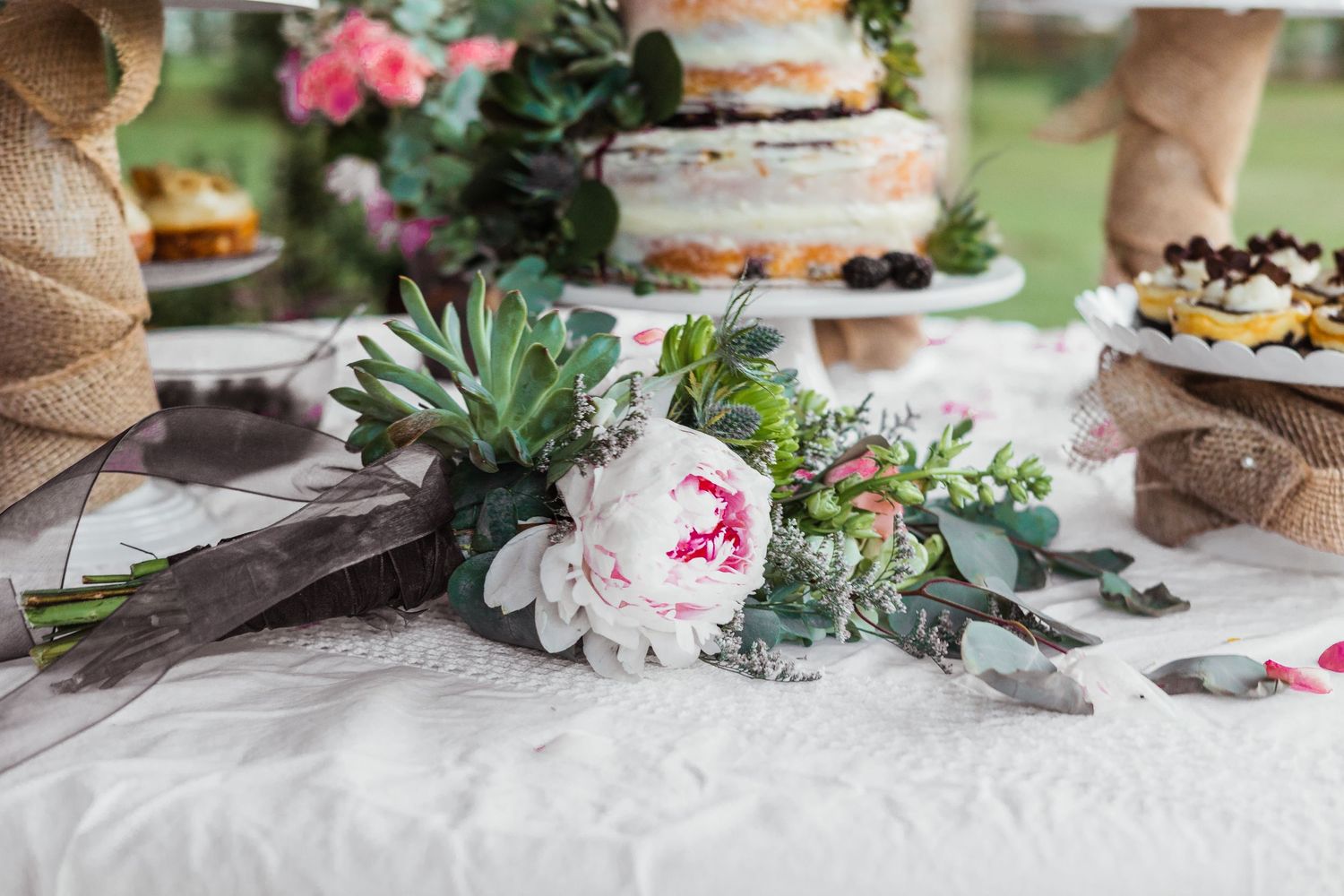 Close-up of wedding dessert table with succulent and peony floral arrangements.
