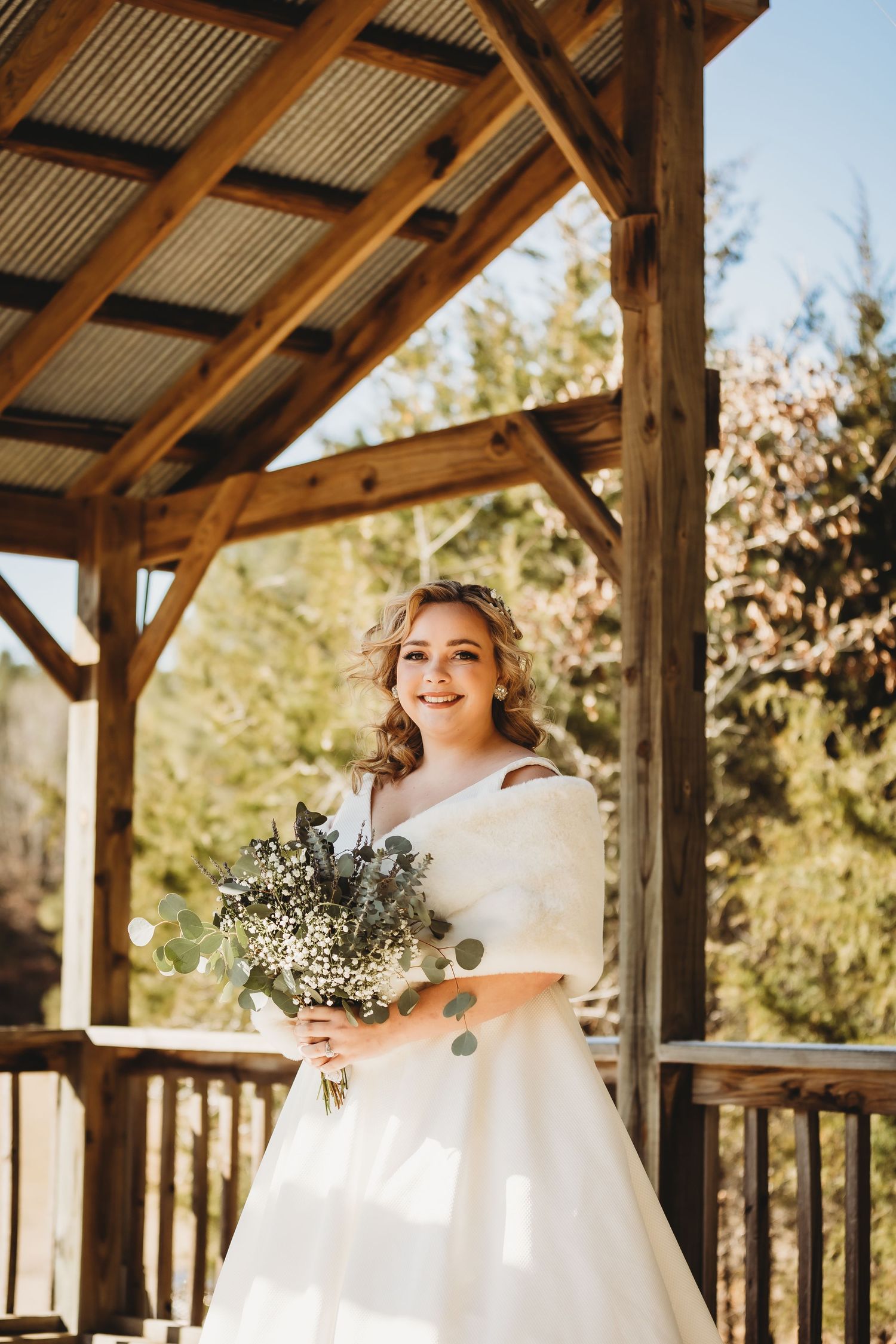 Sunlit bridal portrait under wooden pavilion with rustic architectural details.
