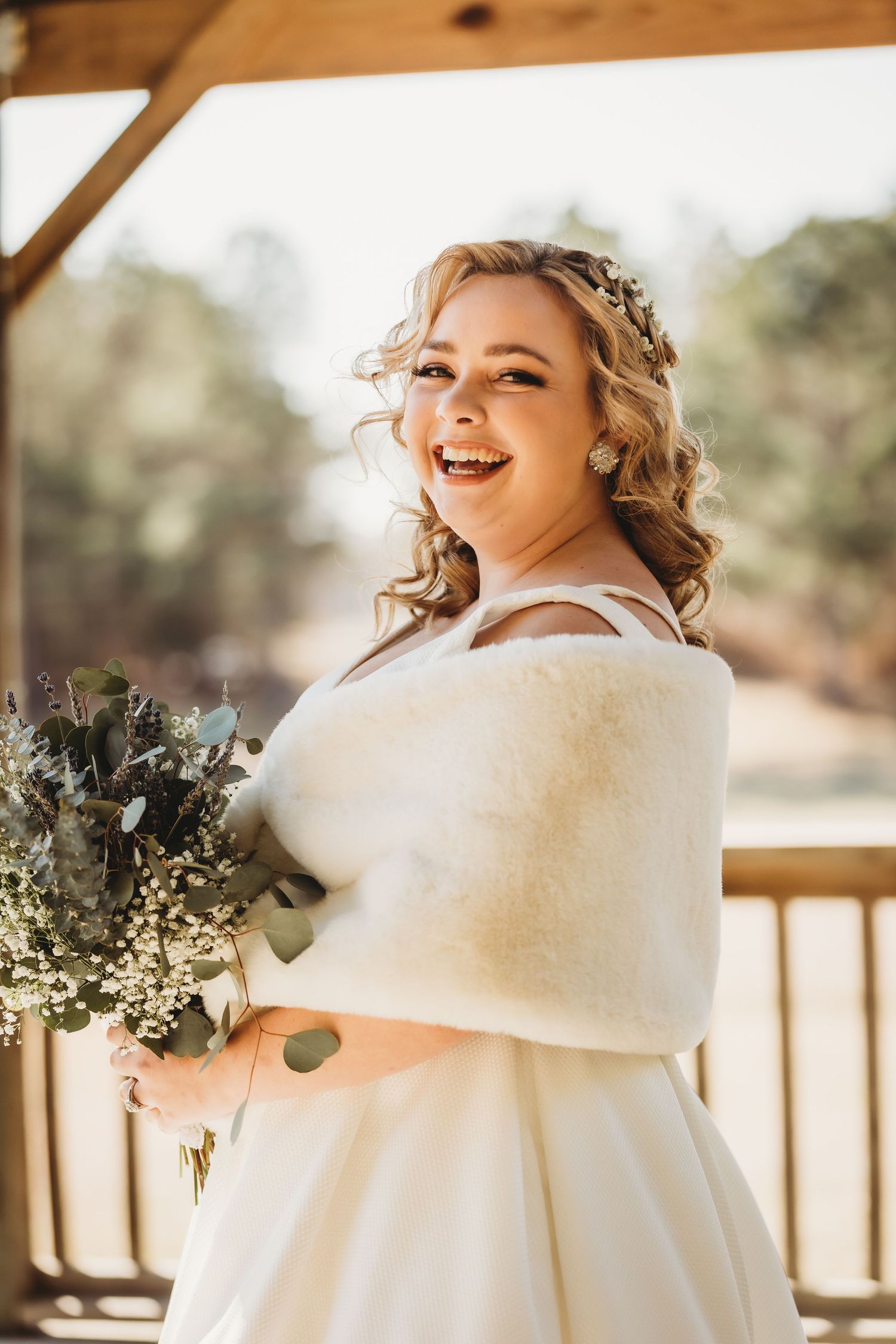 Joyful bridal portrait in natural sunlight wearing a white gown with wrap and floral crown.