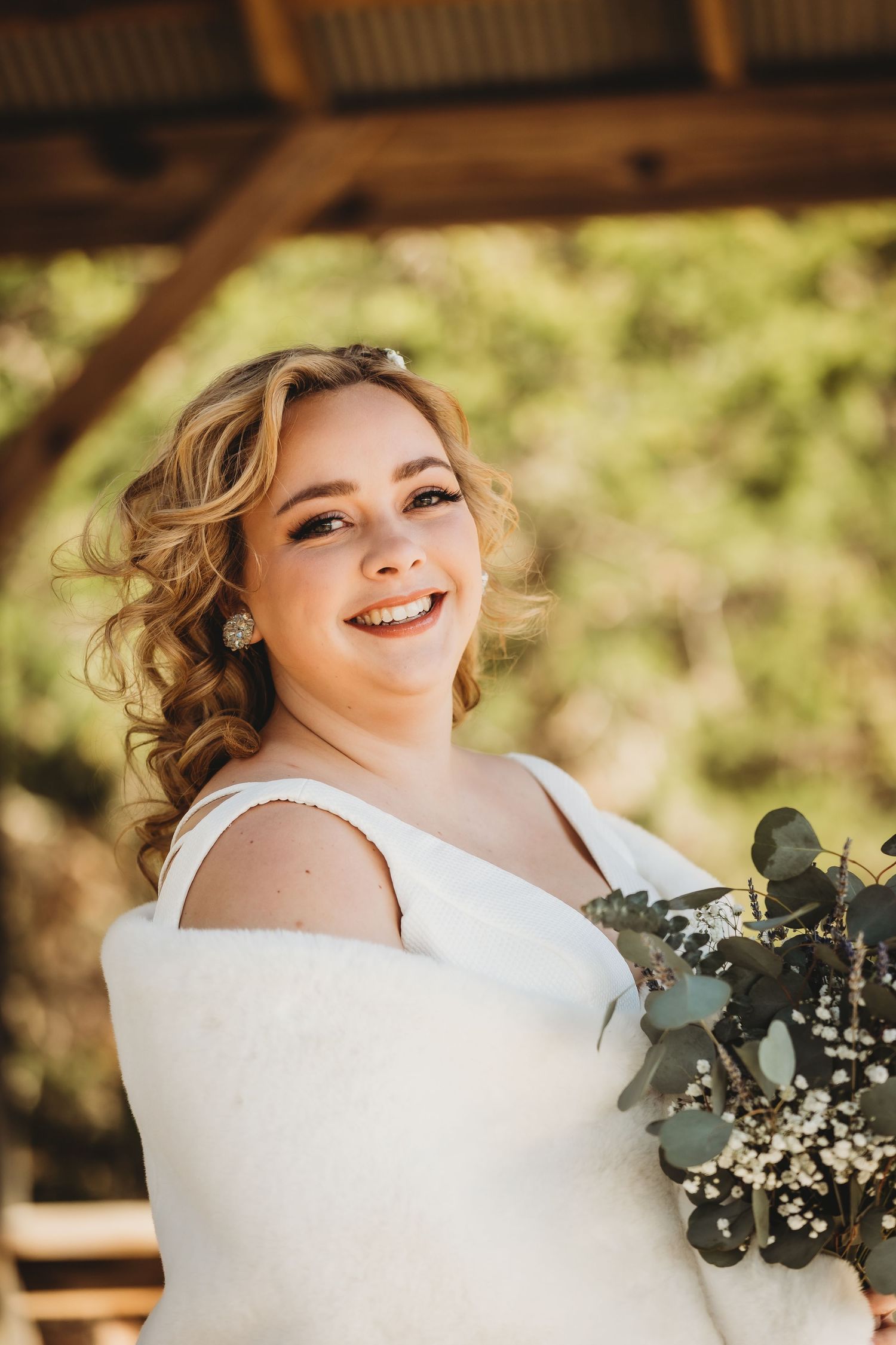 Sun-drenched bridal portrait on wooden deck with natural bouquet and classic white gown.