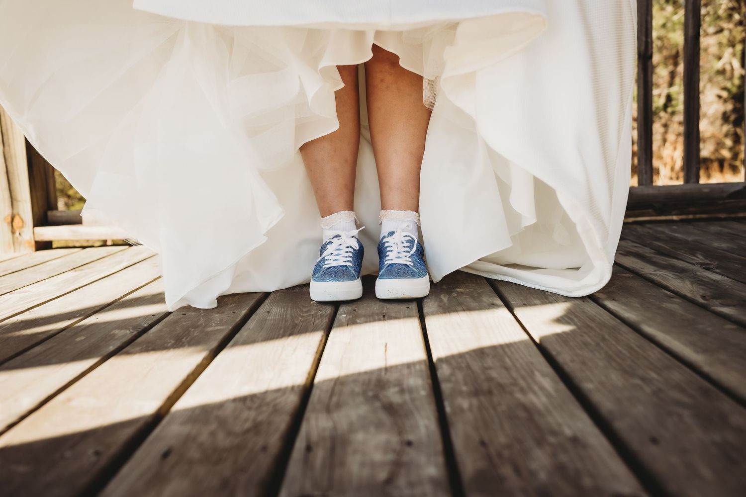 White wedding dress and blue shoes on a rustic wooden deck in natural lighting.