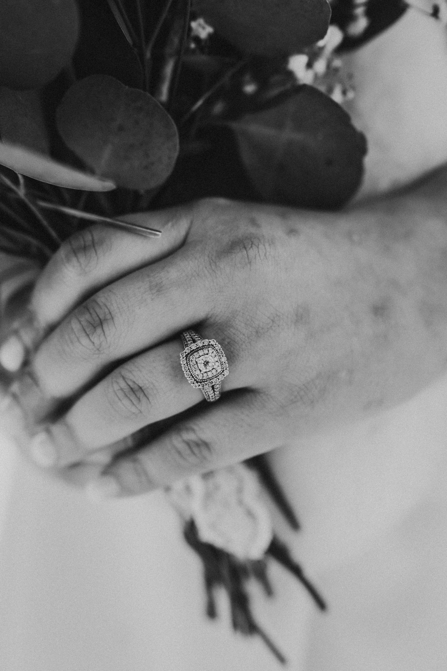 Close-up black and white photo of an elegant engagement ring on a hand.