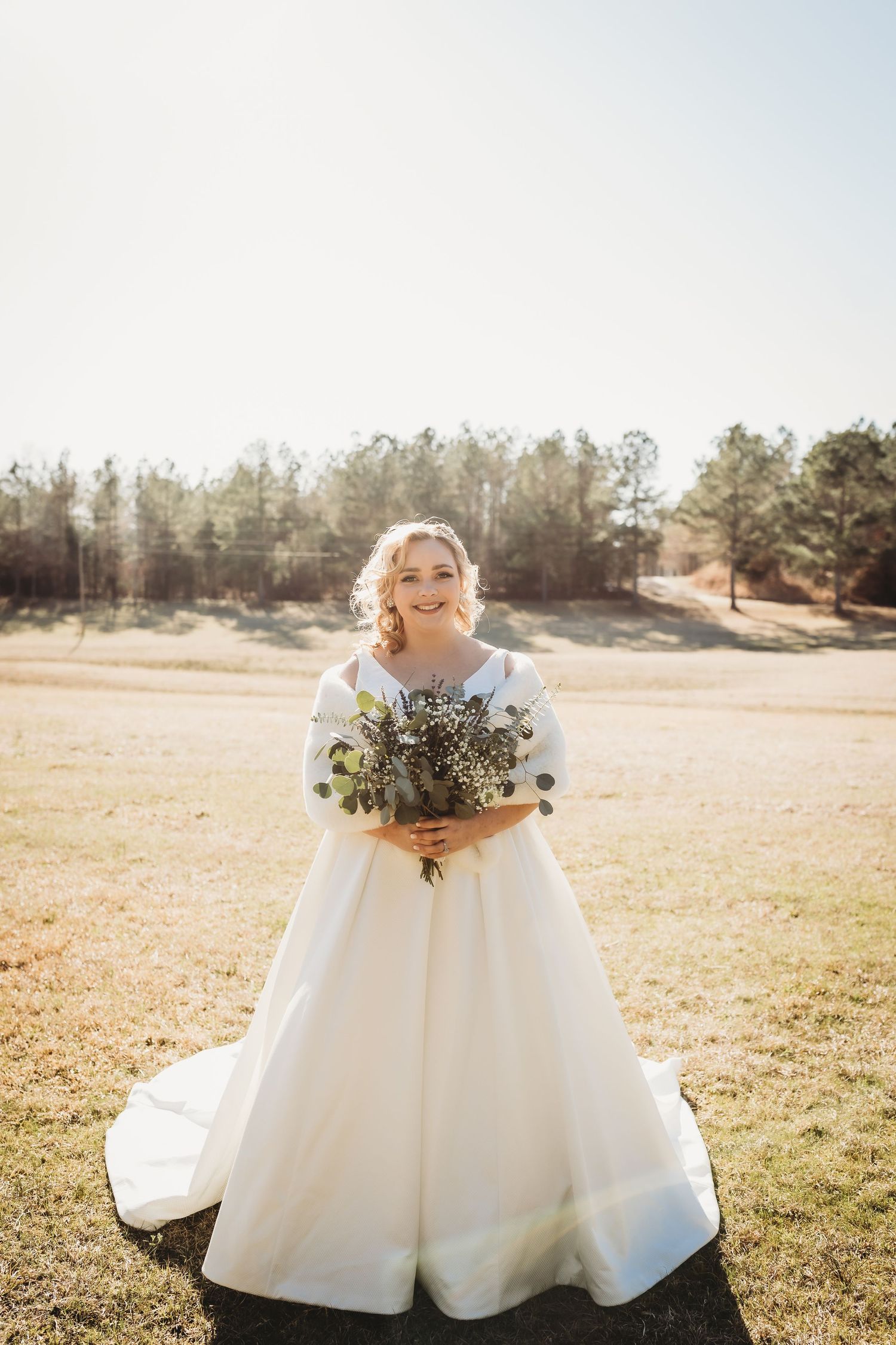 Elegant white wedding dress with a full skirt photographed in a golden field at sunset.