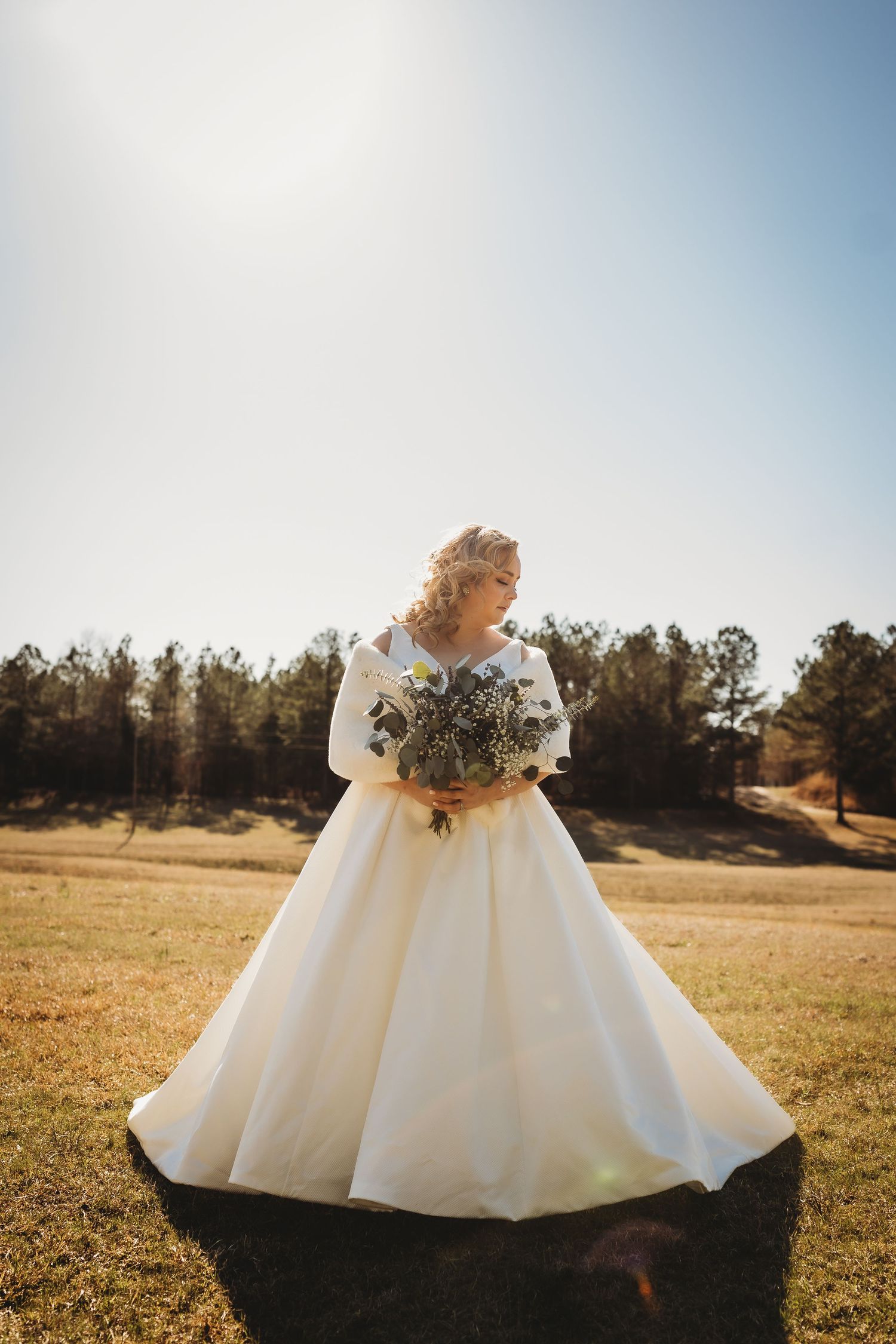 Flowing white wedding gown billowing in a sunlit field with trees in the background.