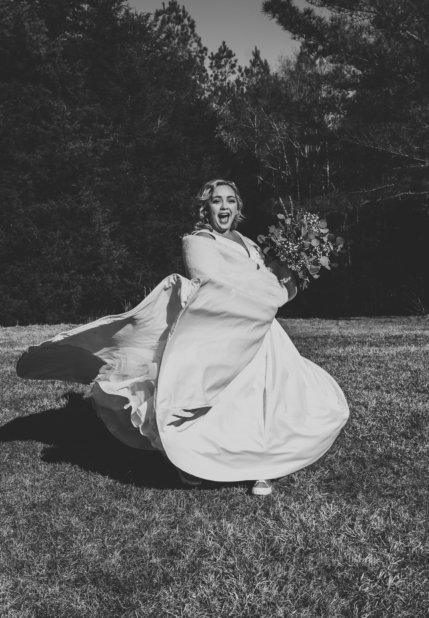 Black and white photo of a bride twirling in her dress on a grassy field.