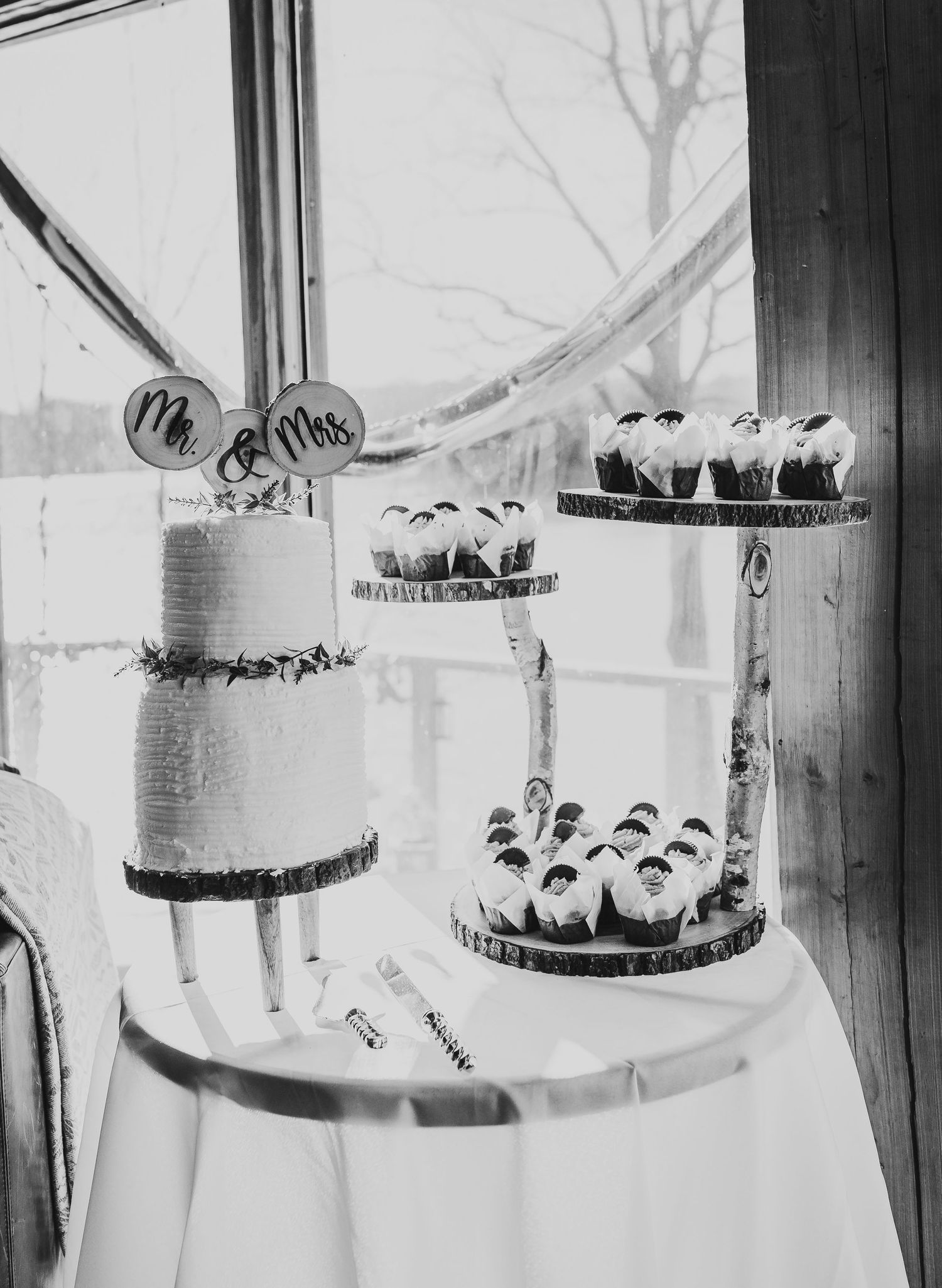A tiered white wedding cake with delicate decorations displayed by a window.