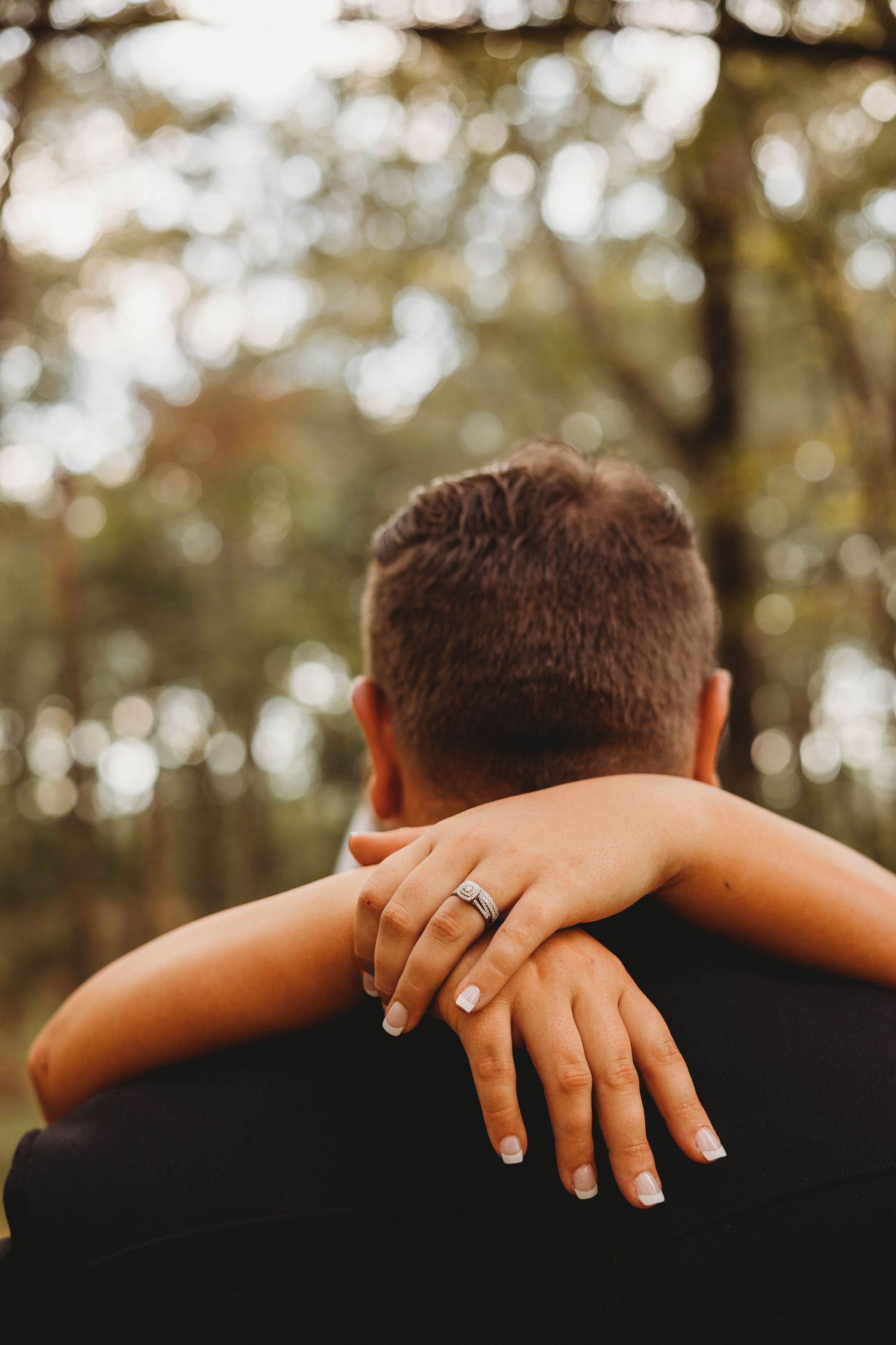 Close-up shot of hands embracing with a wedding ring visible against a blurred natural background.