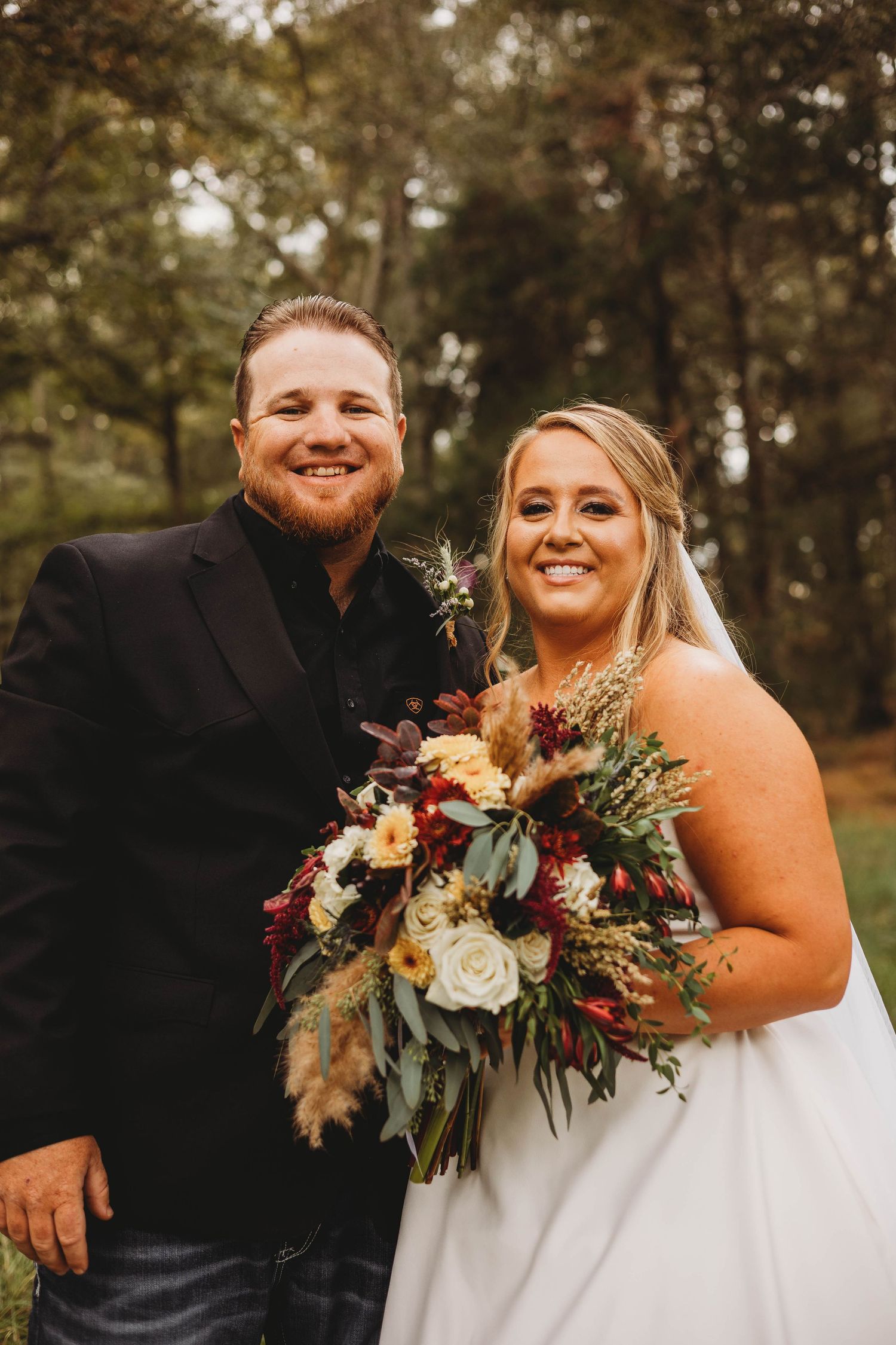 Wedding couple poses outdoors with autumn-colored bouquet featuring burgundy and cream flowers.
