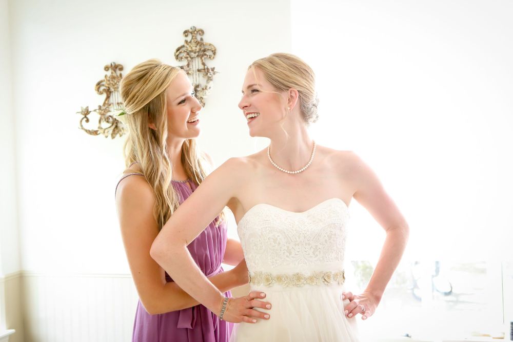 Two women share a candid moment while getting ready in a brightly lit room with elegant decor.