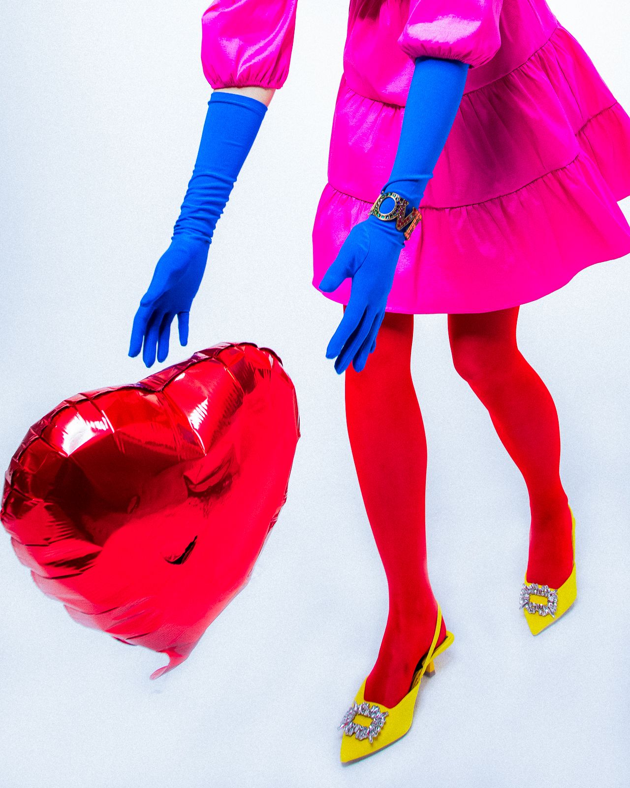 Close-up of pink dress with blue gloves holding red heart balloon and yellow shoes.