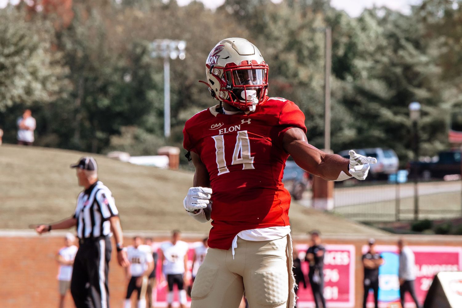 Football player in red jersey number 14 celebrates during game with referee in background.